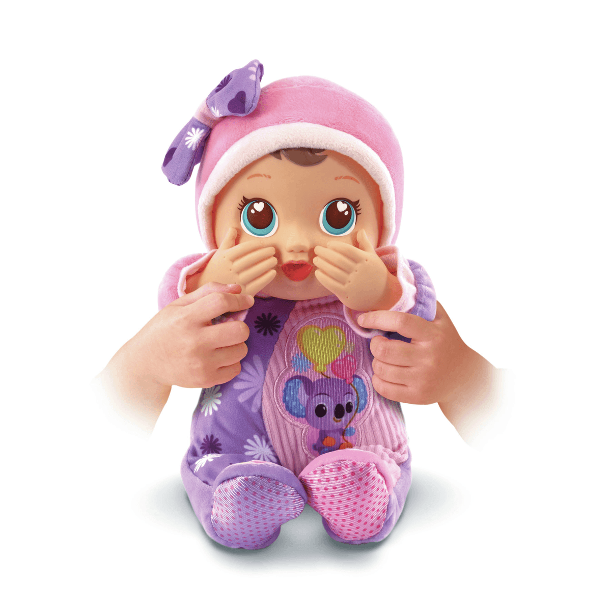 Eine Spielzeugpuppe mit pinker Mütze und lilafarbenem Schlafanzug hält ihre Hände vor das Gesicht.