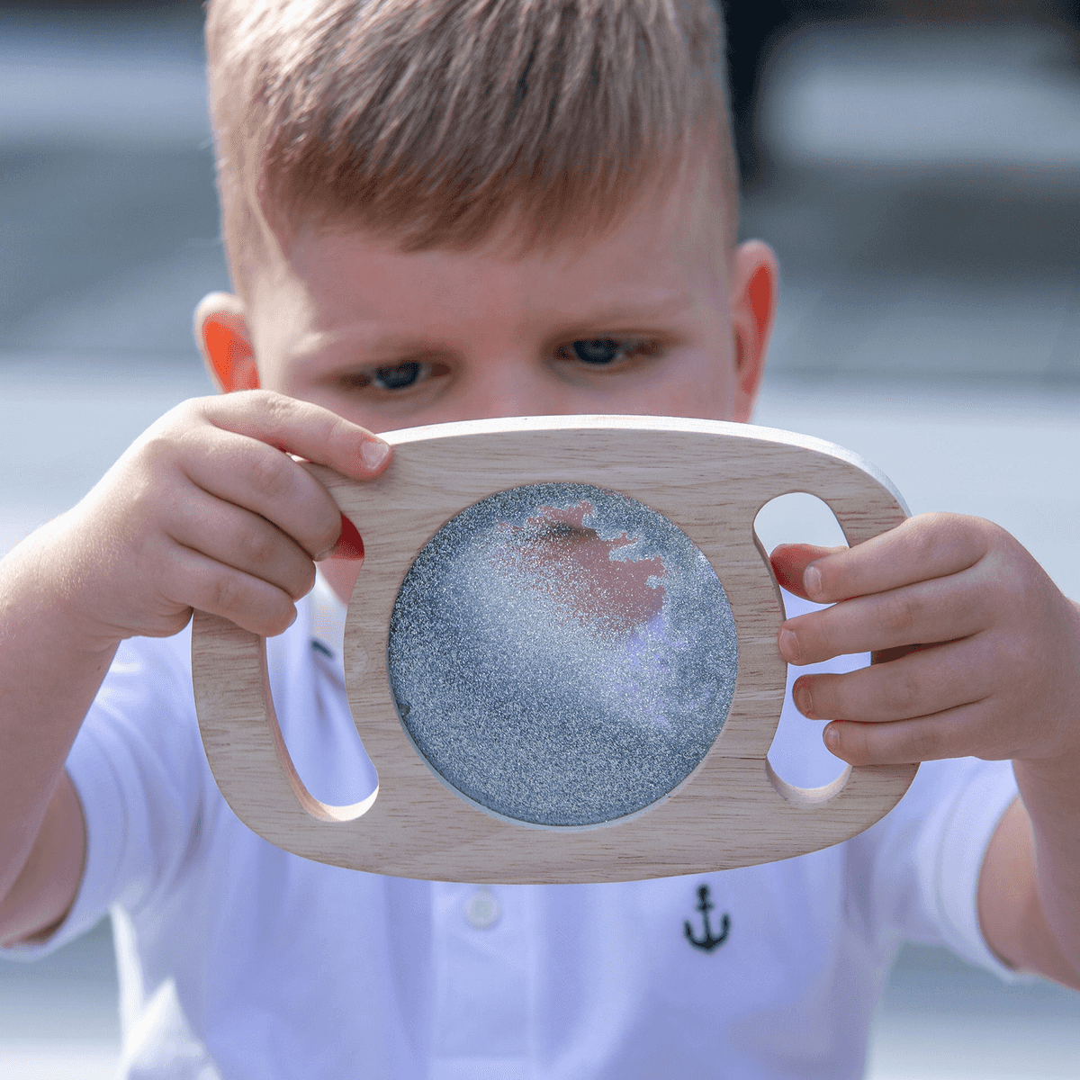 Un niño pequeño sostiene y mira atentamente un juguete sensorial de madera con líquido brillante.
