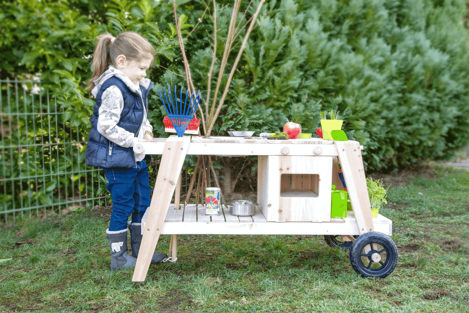 Un niño pequeño juega al aire libre en un jardín con un banco de jardinería de juguete.