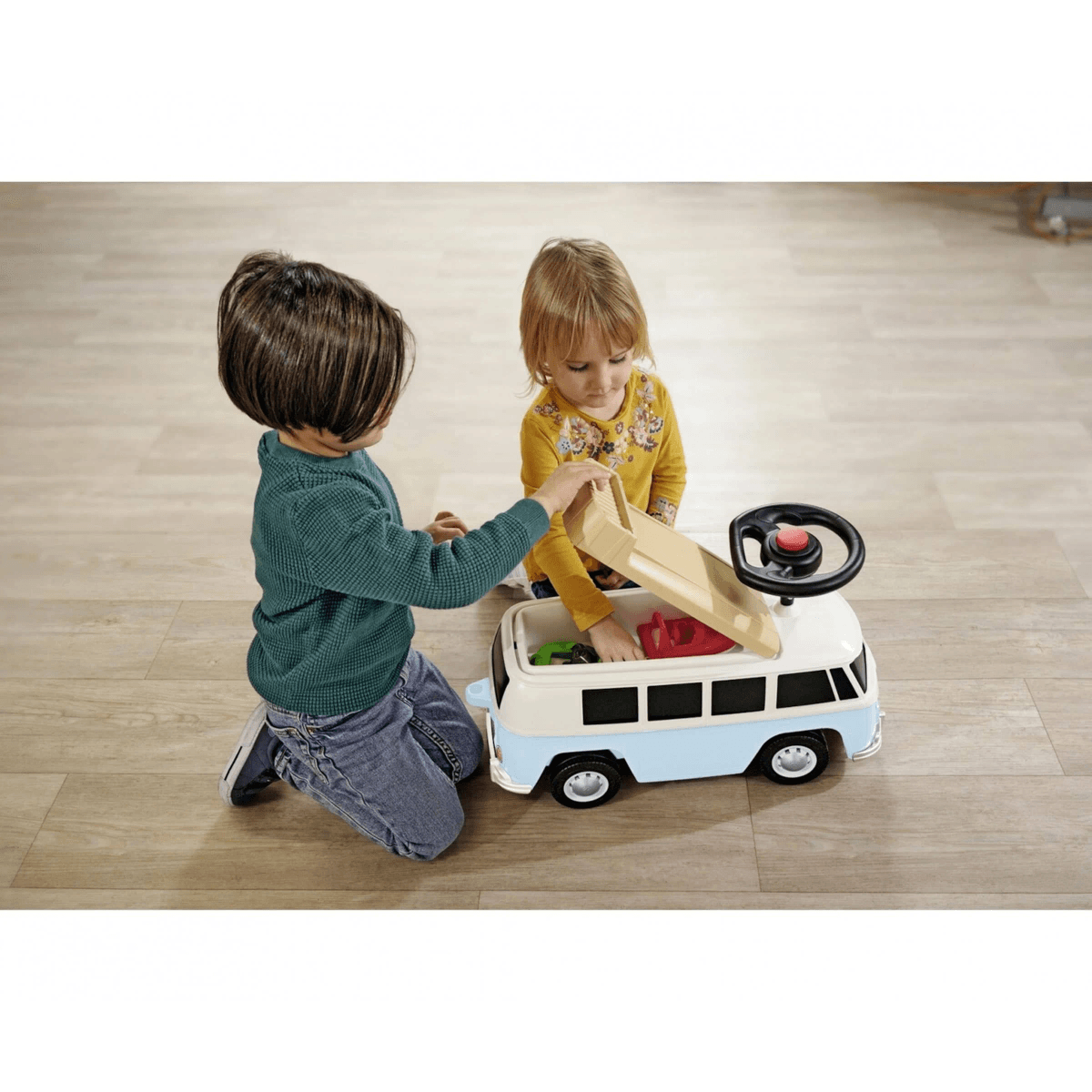 Dos niños se arrodillan en un suelo de madera, jugando con una furgoneta de juguete azul y blanca.