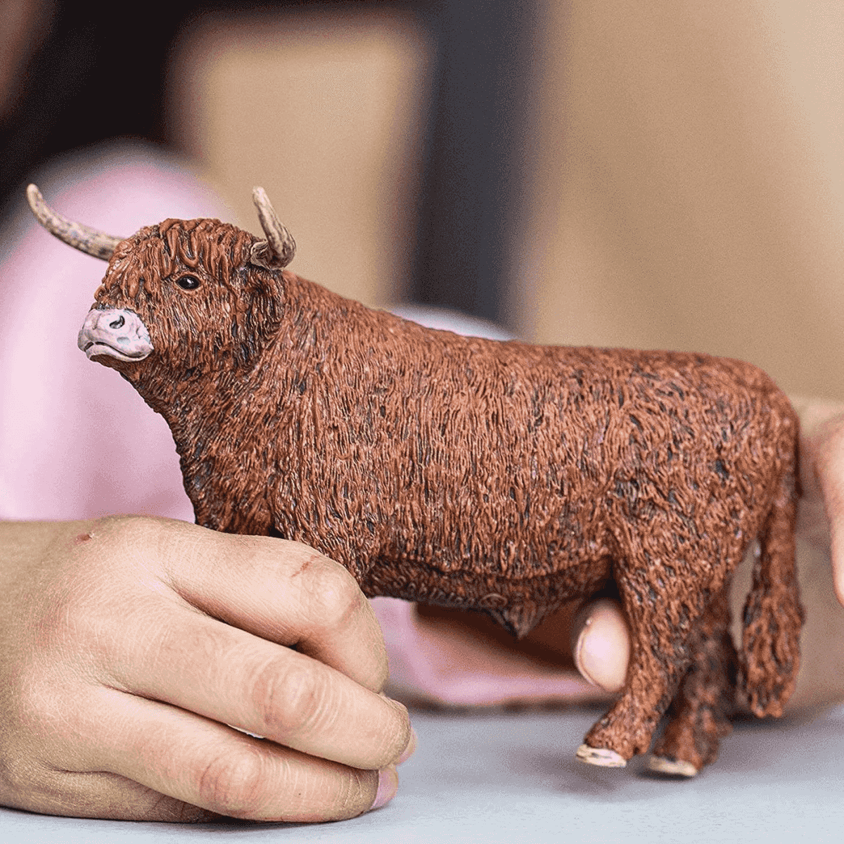 Eine kleine braune Hochlandrind-Figur wird sanft in Händen gehalten.