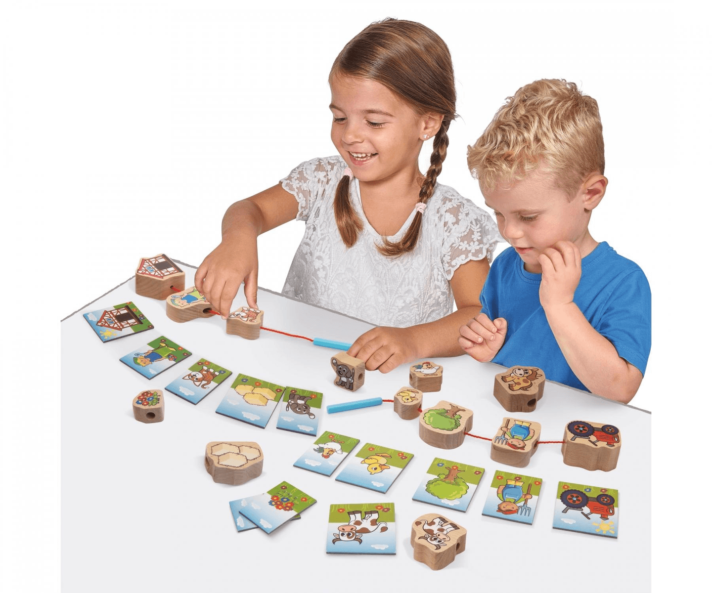 Ein Junge und ein Mädchen sitzen am Tisch und fädeln Holzklötze mit Bauernhofmotiven auf Schnüre.