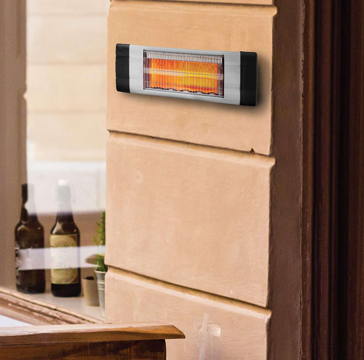 Ein elektrischer Heizstrahler leuchtet orange und hängt an einer beigen Wand neben einem Fenster.