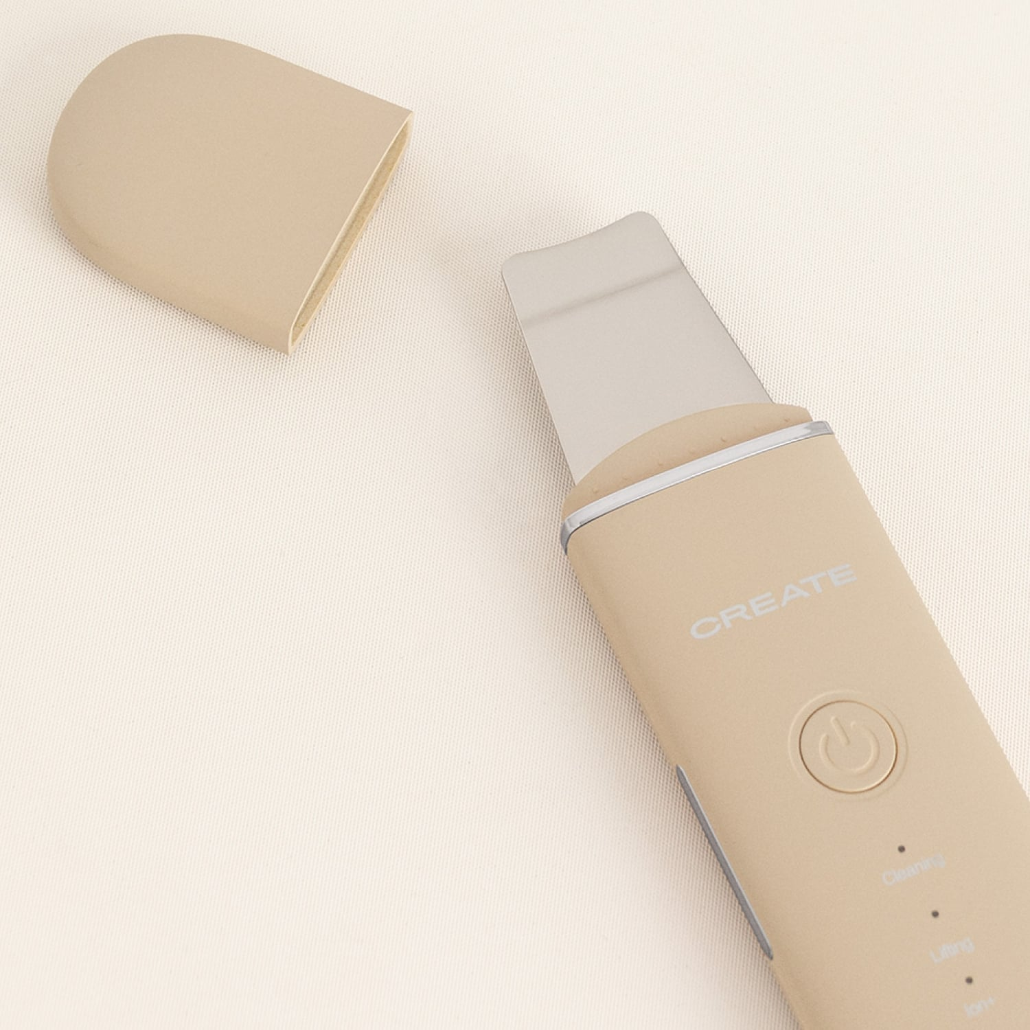 Espátula ultrasónica de piel beige con tapa retirada sobre fondo beige.