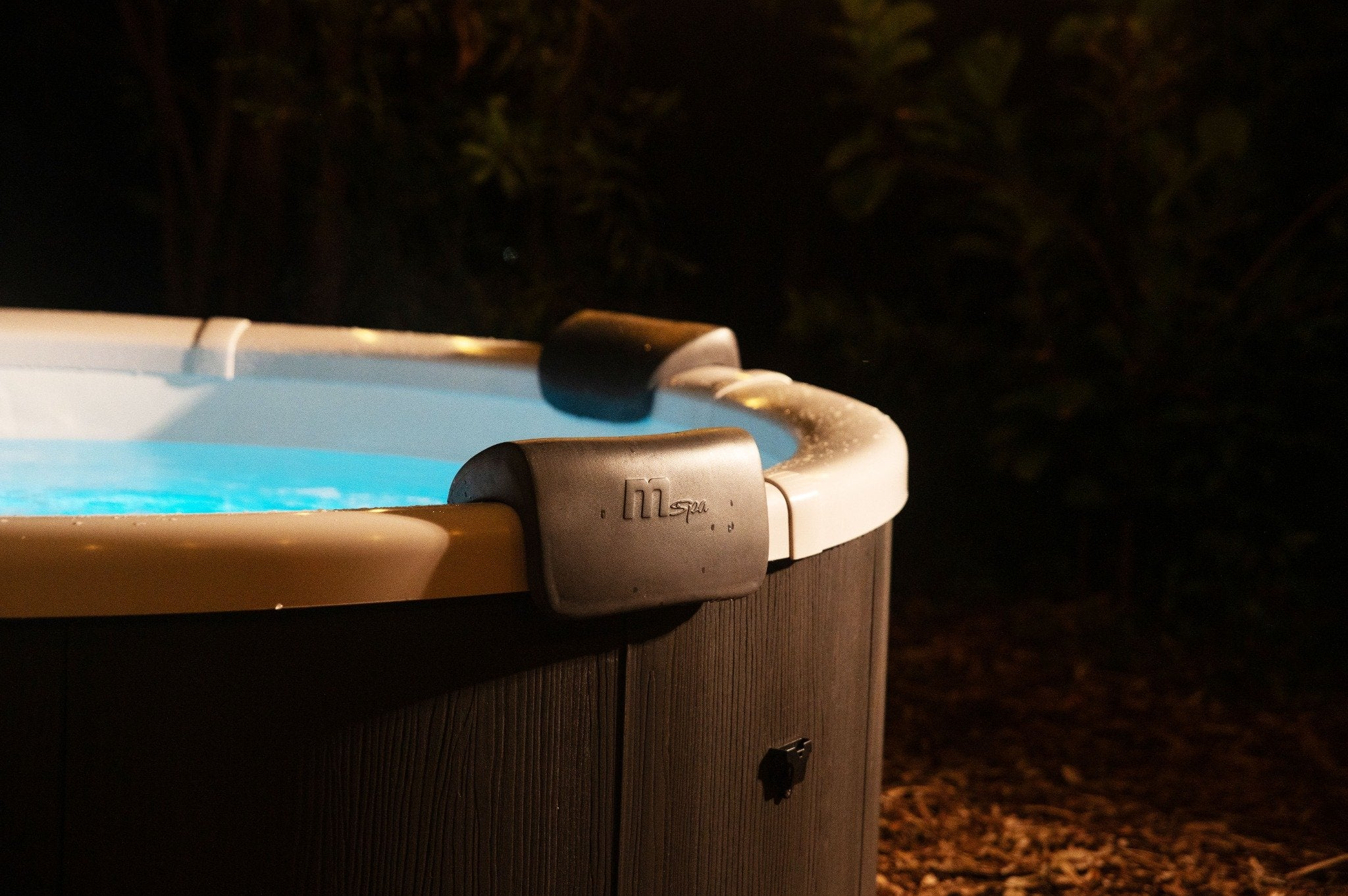 Bañera de hidromasaje iluminada al aire libre de noche con paneles de madera.