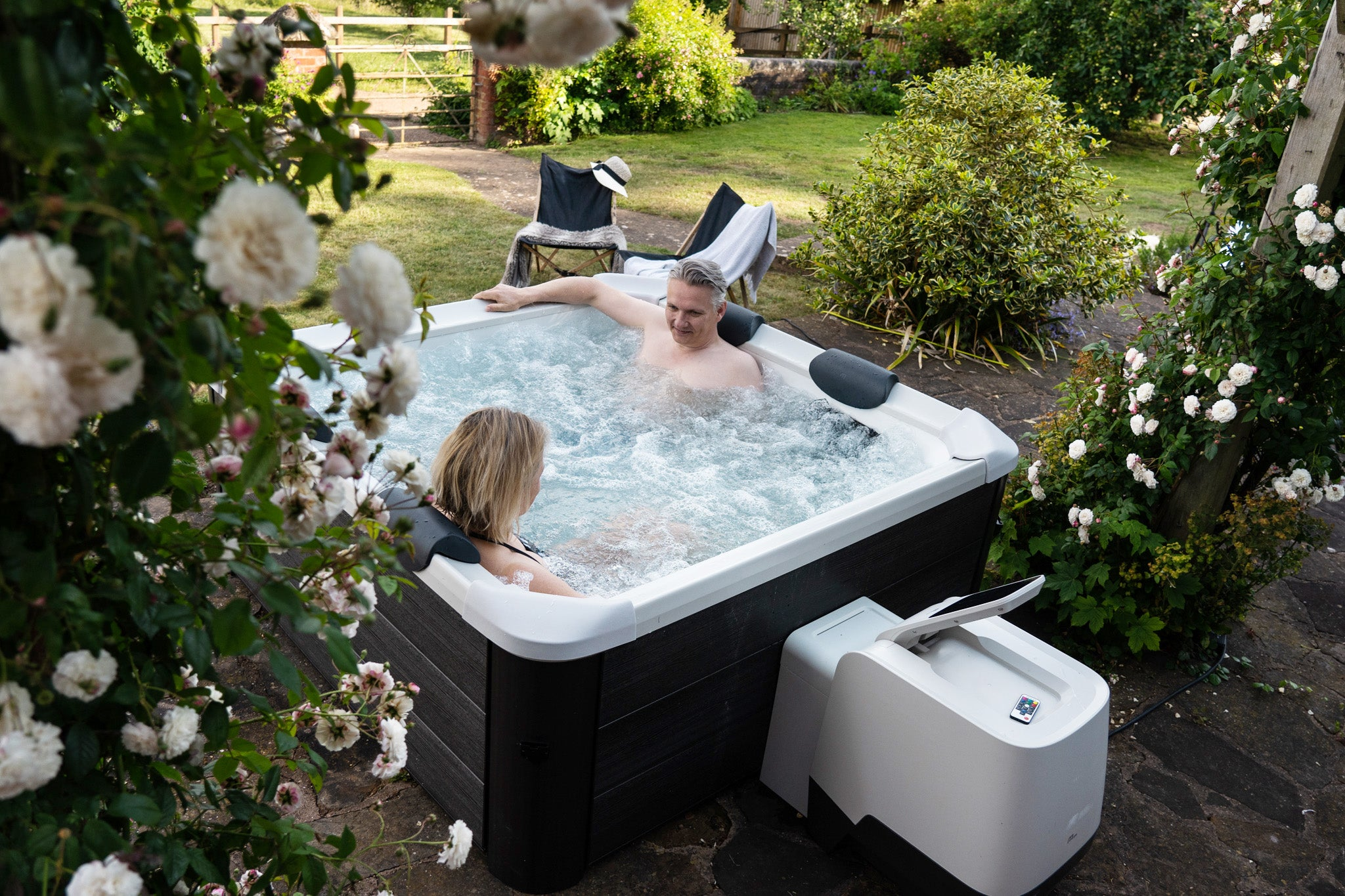 Una pareja se sienta en un jacuzzi en un jardín verde, rodeada de rosales.