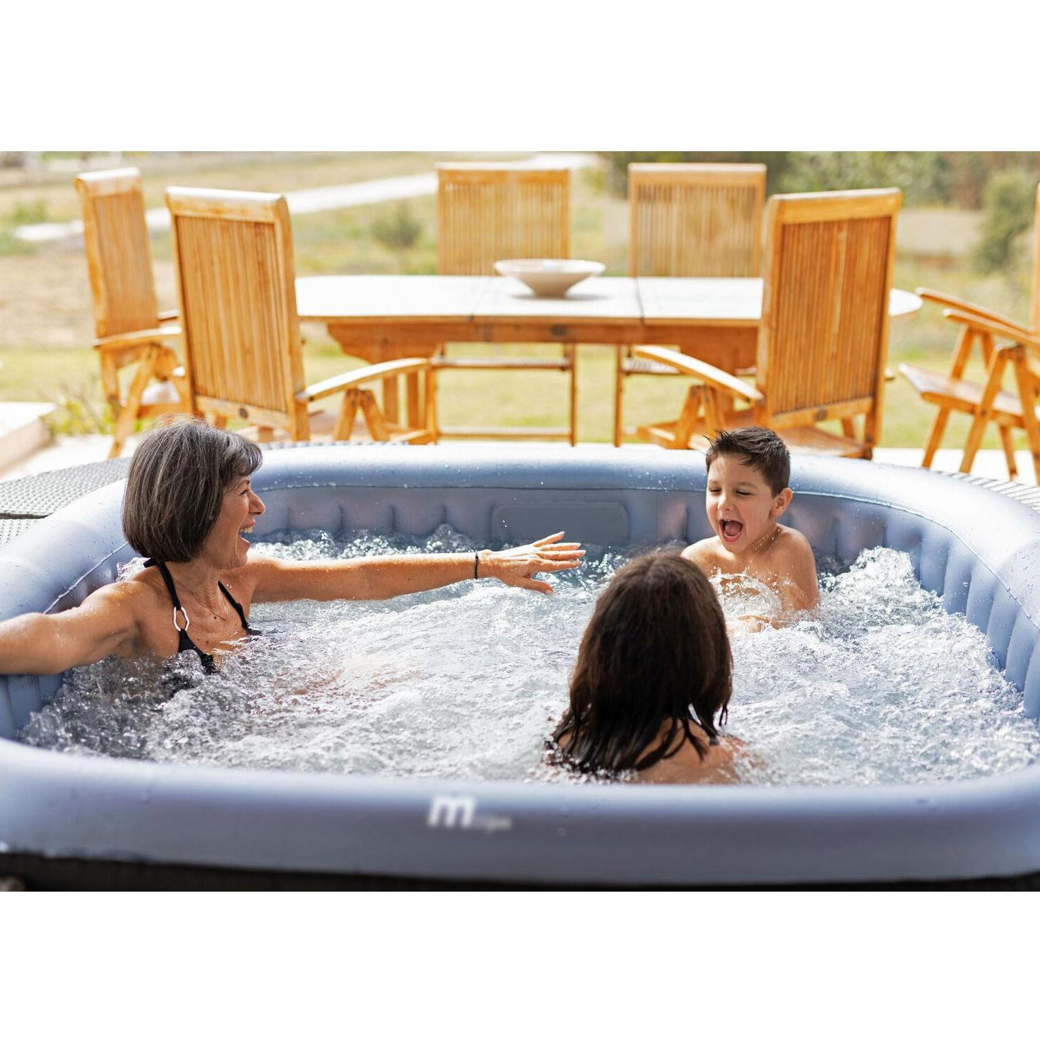 Una mujer y dos niños disfrutan de un jacuzzi inflable burbujeante al aire libre en un día soleado con muebles.