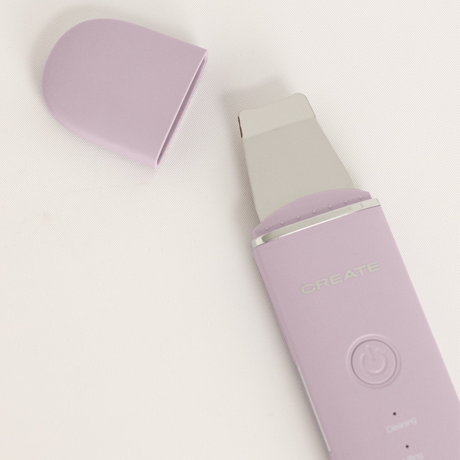 Un dispositivo limpiador facial morado con punta de metal y tapa protectora retirada sobre superficie clara.