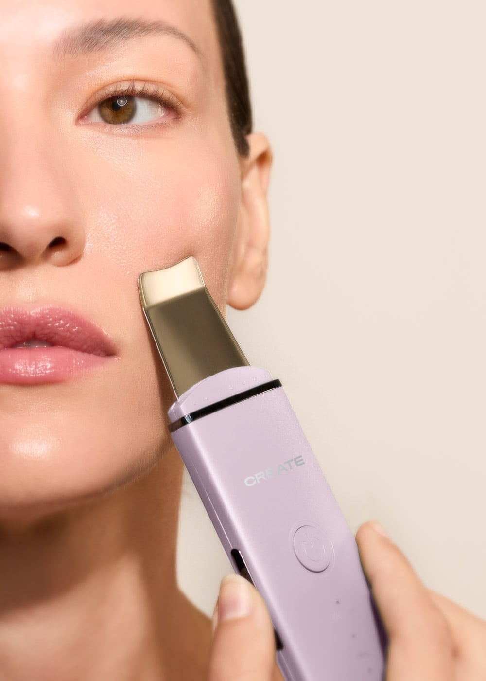 Una persona usa una espátula de limpieza facial morada en su mejilla.