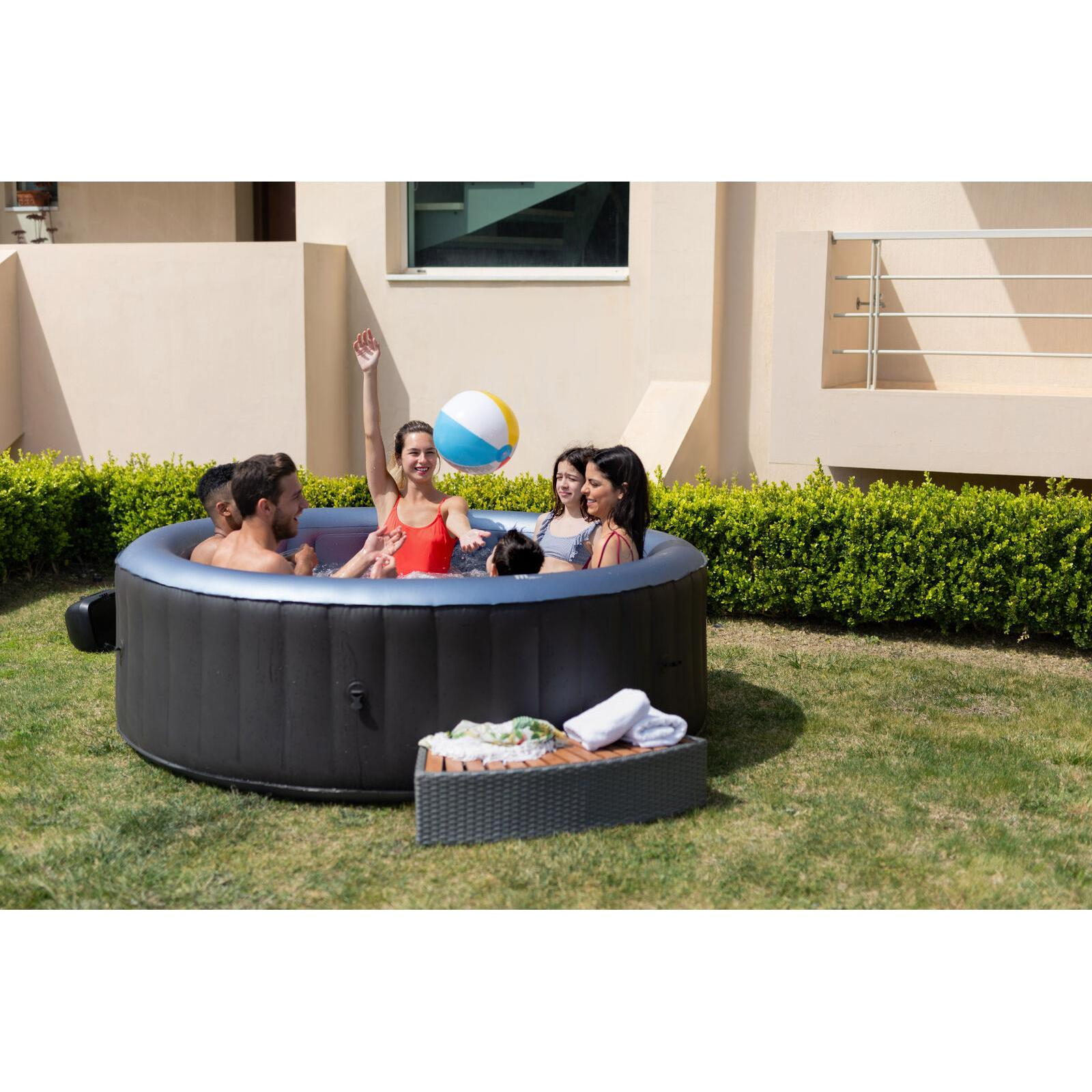 Familia jugando con una pelota de playa en un jacuzzi negro redondo en el césped frente a la casa.