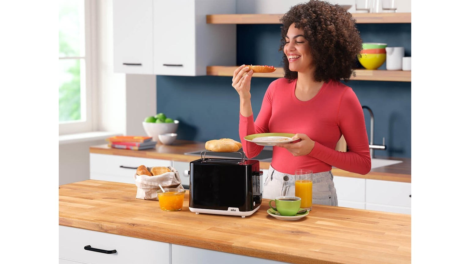 Una mujer en una cocina sostiene tostadas con mermelada, junto a una tostadora negra en una encimera de madera.