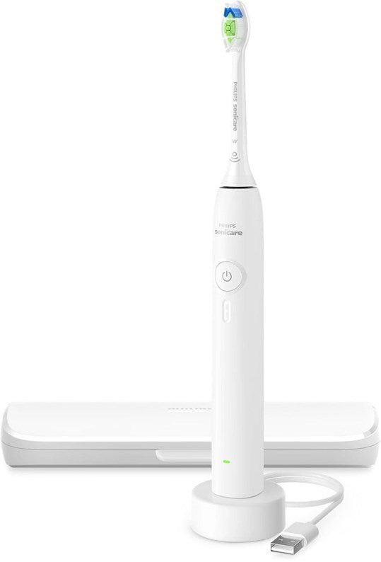 Un cepillo de dientes eléctrico Philips Sonicare blanco en su base de carga con cable USB y estuche de viaje al fondo.