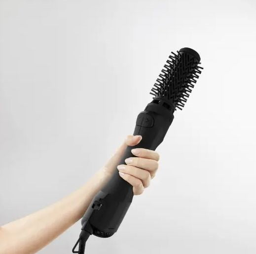 Eine Hand hält eine schwarze Haarstyling-Bürste vor einem hellgrauen Hintergrund.