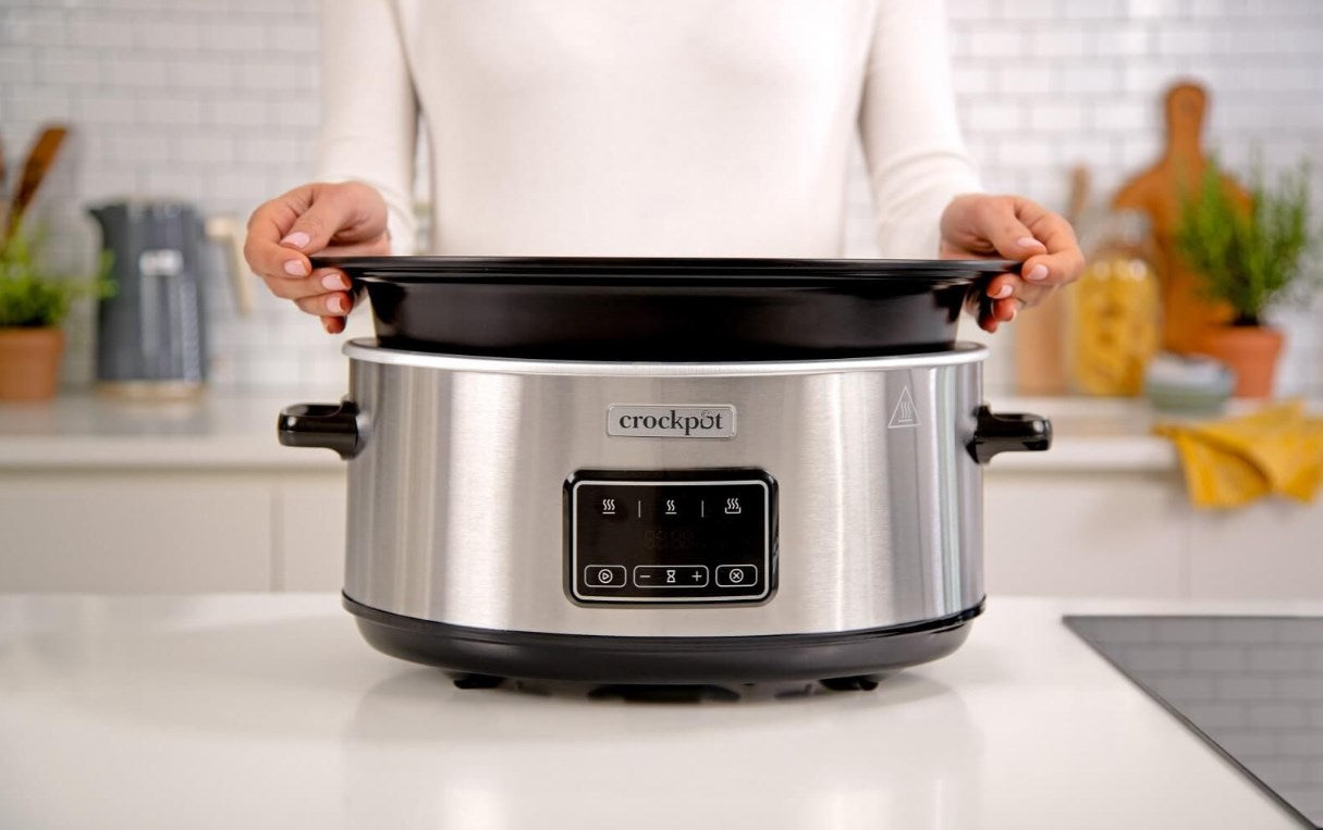Una persona inserta la olla negra en un Crockpot plateado sobre una encimera de cocina blanca.