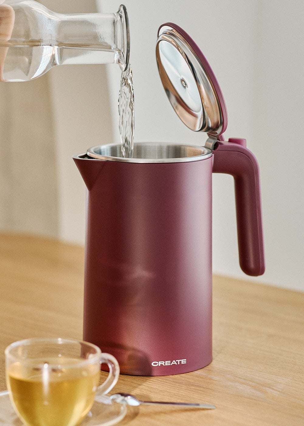 Se vierte agua de una botella de cristal en un hervidor rojo sobre una mesa de madera.