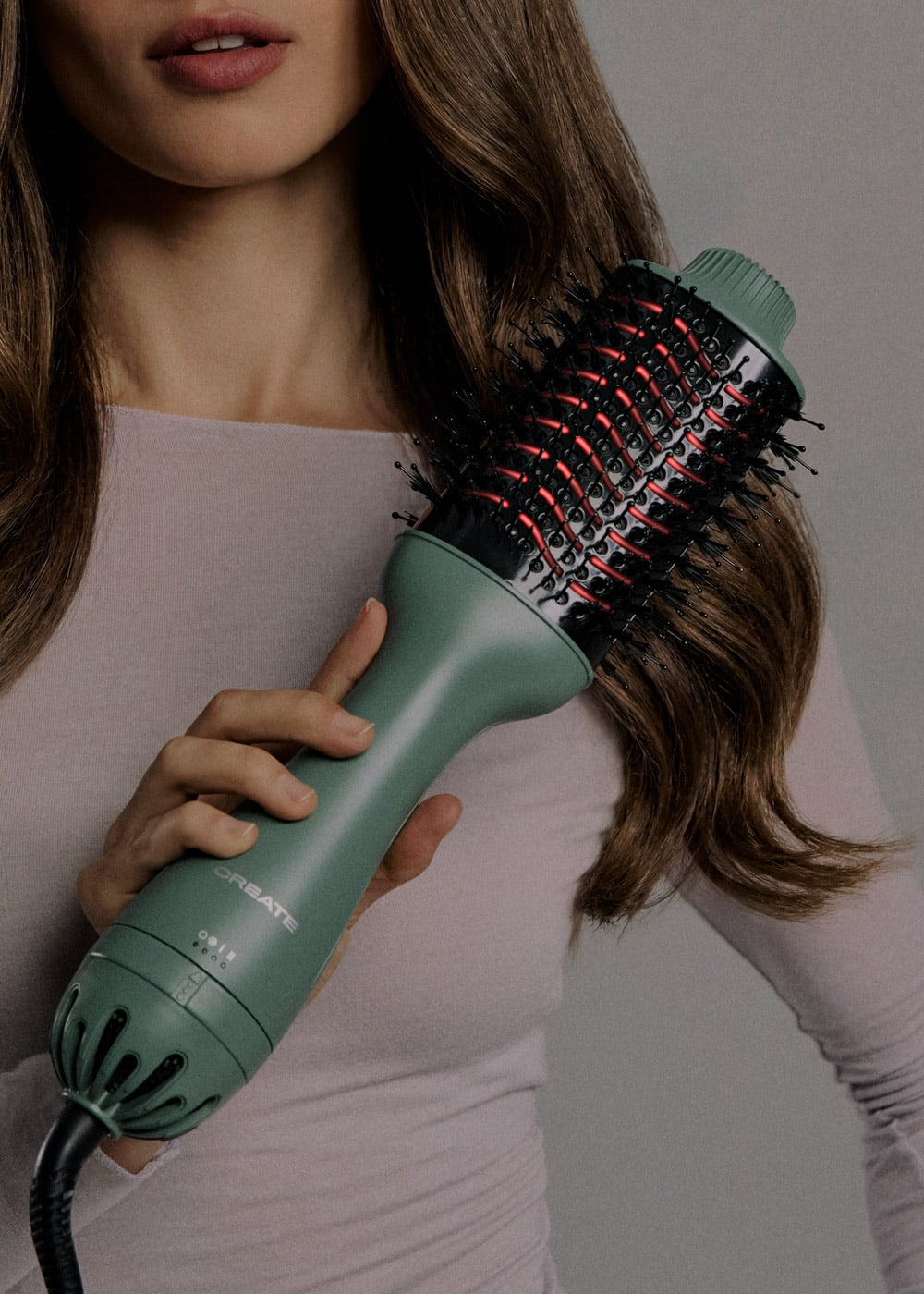 Una mujer sostiene un cepillo secador de pelo verde con cerdas negras y rojas.