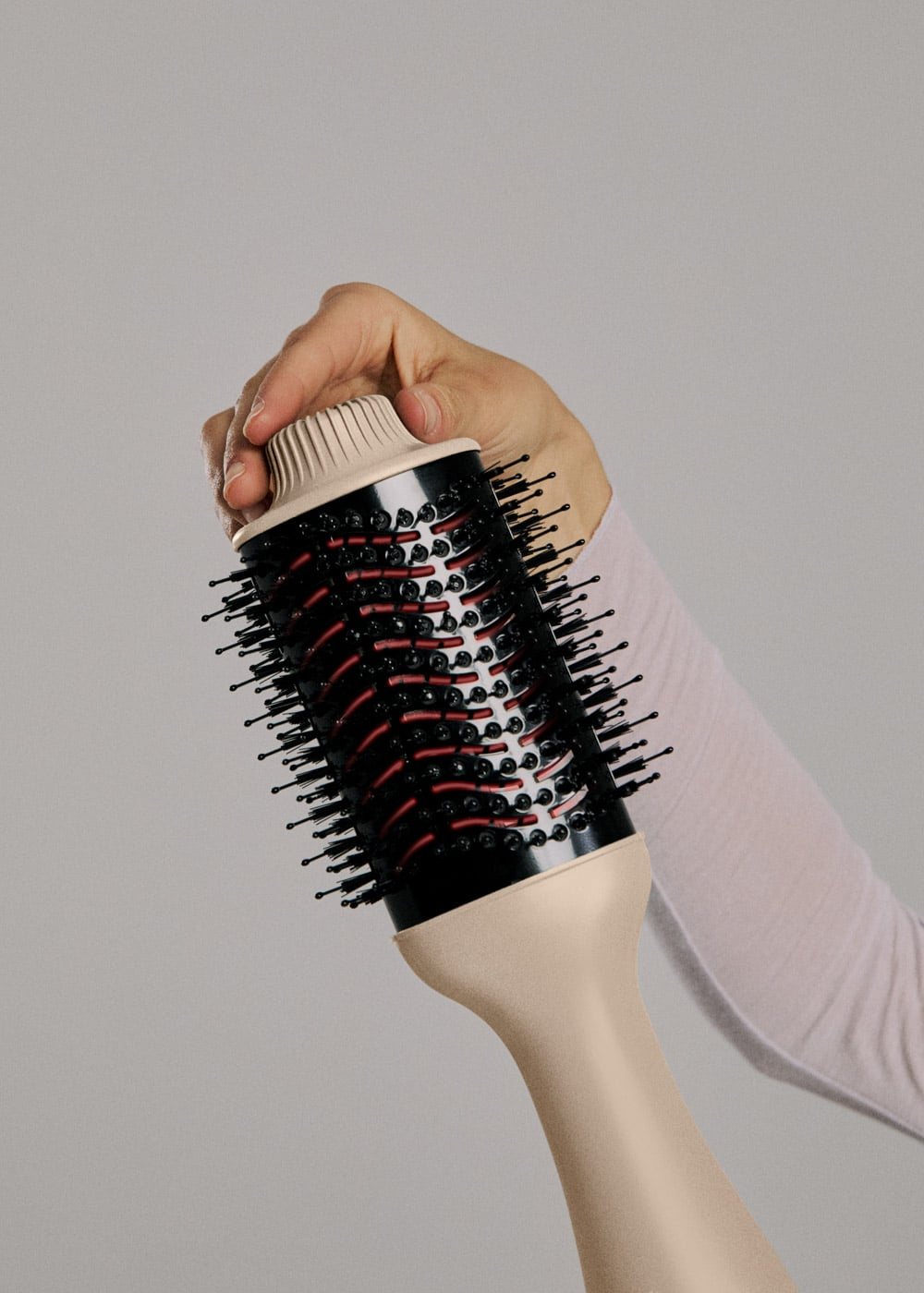 Una mano sostiene un cepillo de pelo negro y beige con cerdas sobre fondo gris.