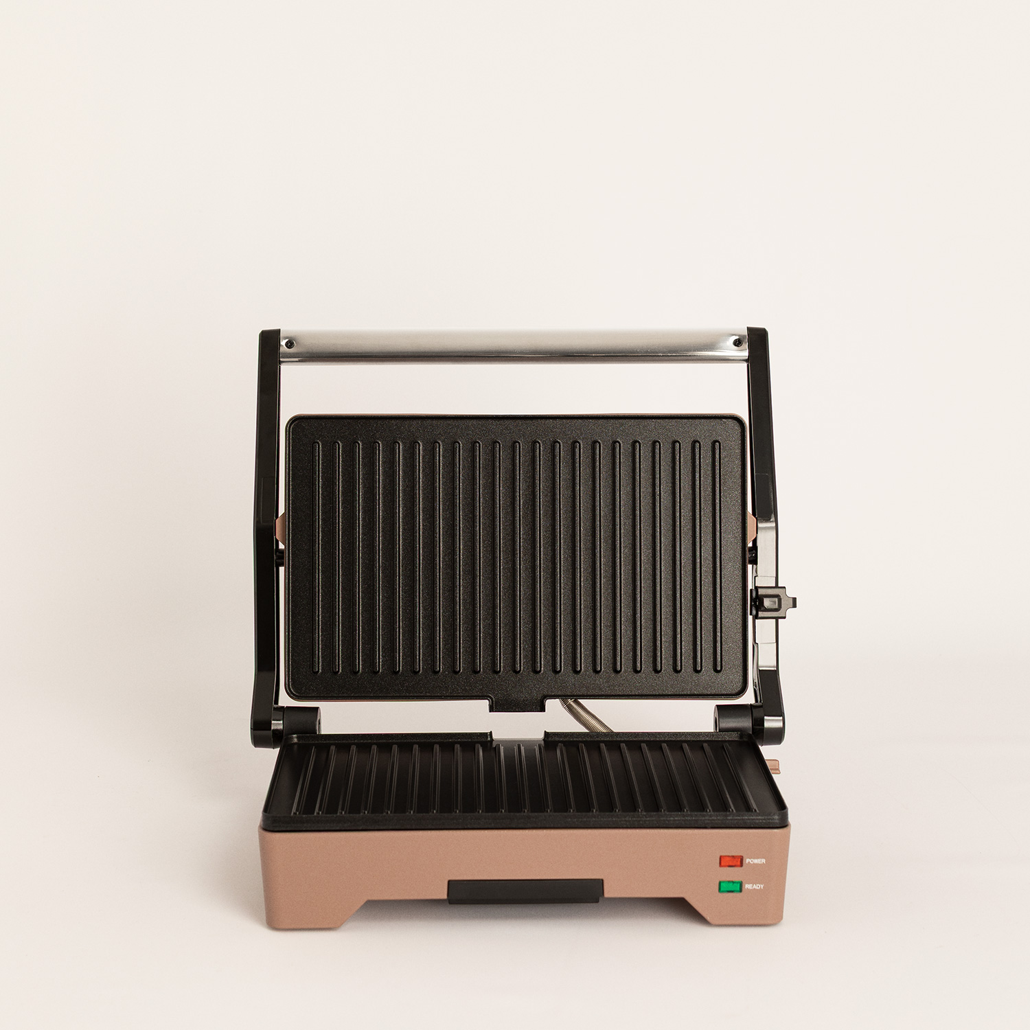 Un grill eléctrico abierto con cuerpo de oro rosa y placas estriadas negras sobre un fondo blanco.