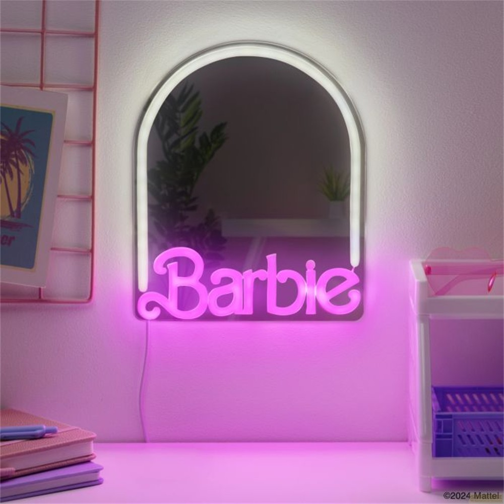 Un espejo iluminado de Barbie con luz de neón blanca y rosa cuelga en una pared sobre un escritorio rosa.