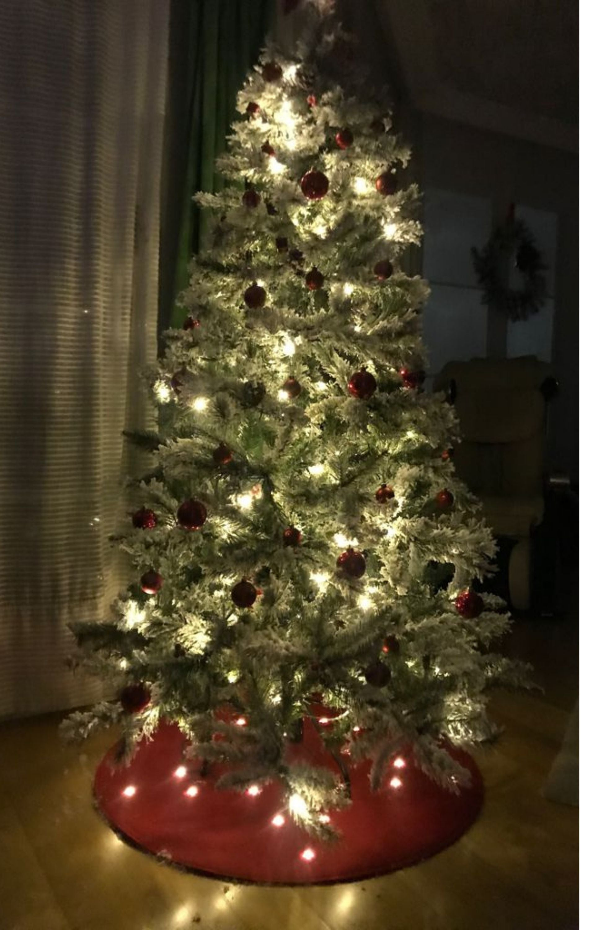Un árbol de Navidad iluminado y cubierto de nieve con adornos rojos en una sala.