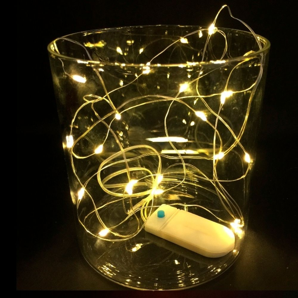 Una cadena de luces LED blancas cálidas dentro de un recipiente de vidrio sobre fondo oscuro.