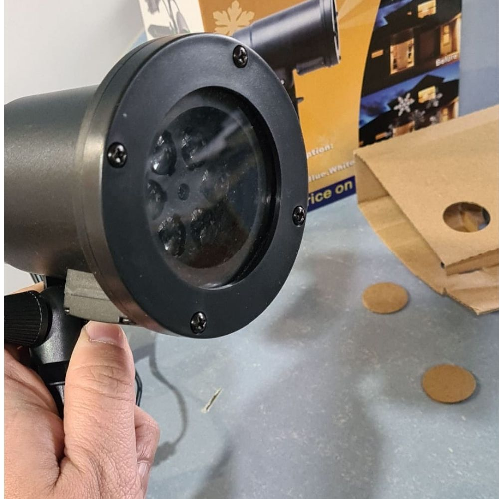 Una mano sostiene un proyector de luz exterior negro, con su caja de producto y cartón de fondo.