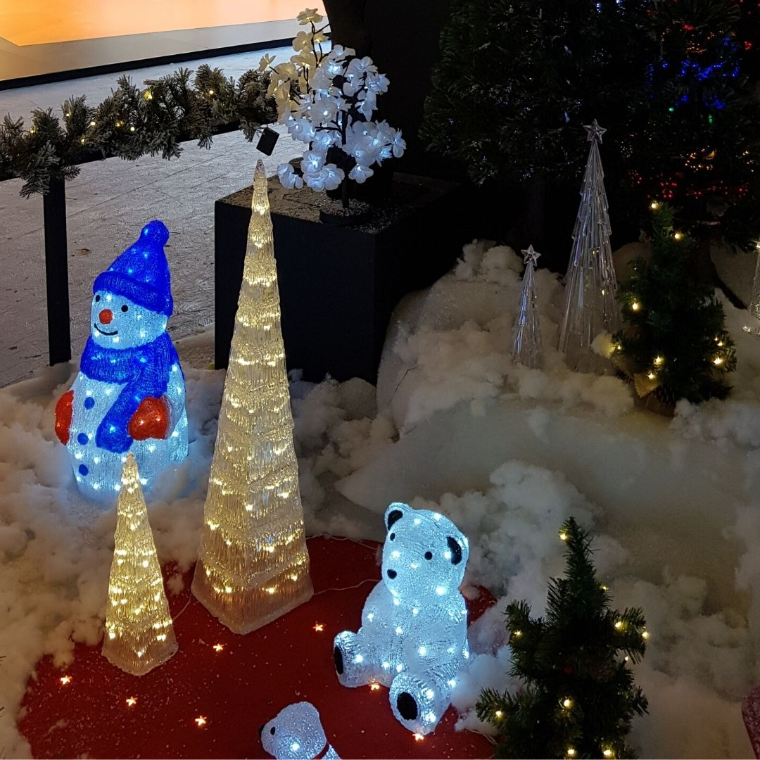 Exposición navideña con muñeco de nieve luminoso, árboles iluminados y un oso polar brillante.