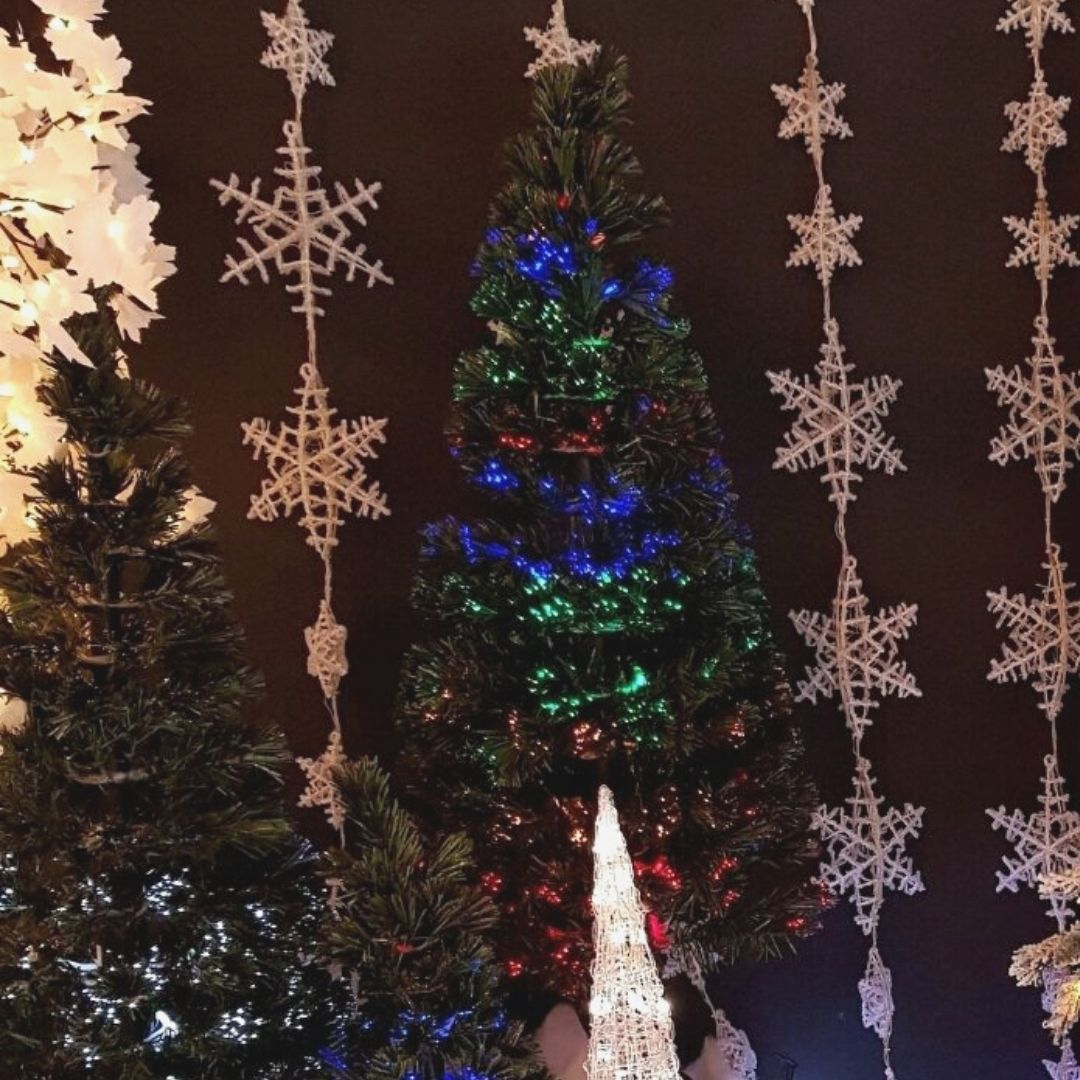 Un árbol de Navidad iluminado con luces azules y verdes, rodeado de guirnaldas de copos de nieve.