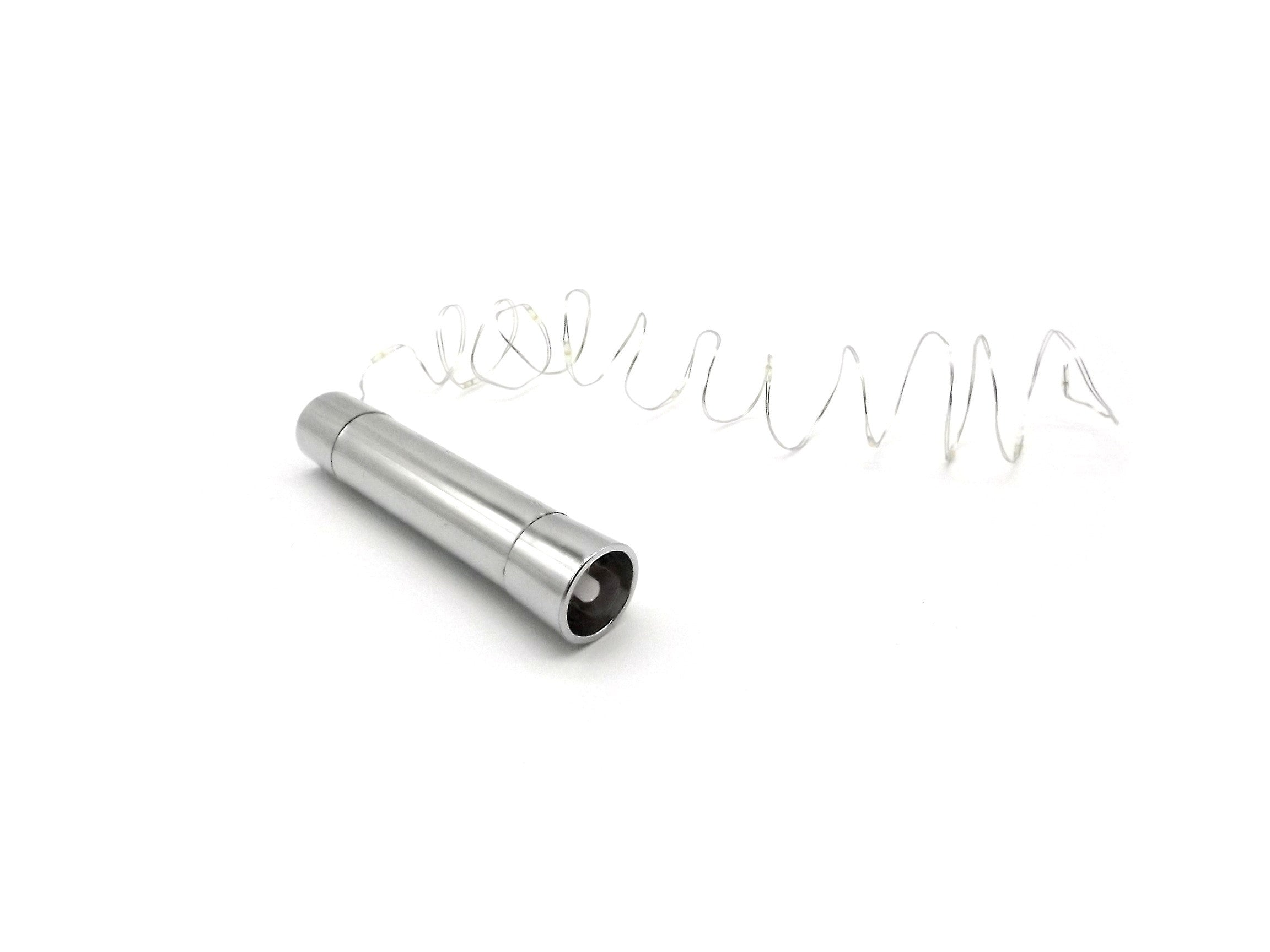 Una linterna cilíndrica plateada yace junto a una cadena de luces enrollada en espiral sobre fondo blanco.