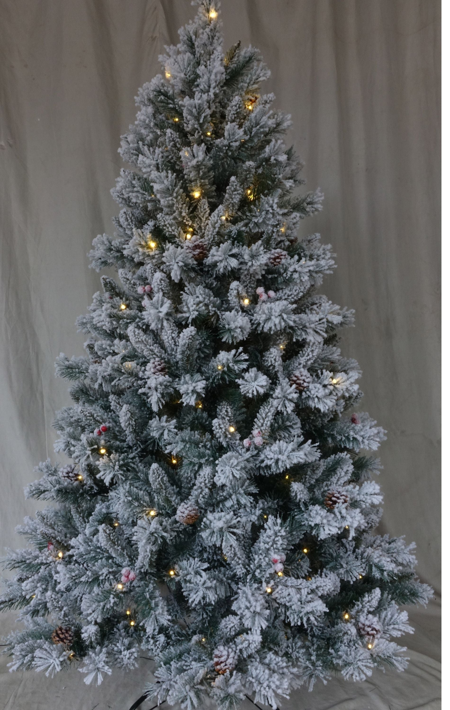 Un árbol de Navidad cubierto de nieve con luces cálidas, piñas y bayas rojas sobre un fondo neutro.