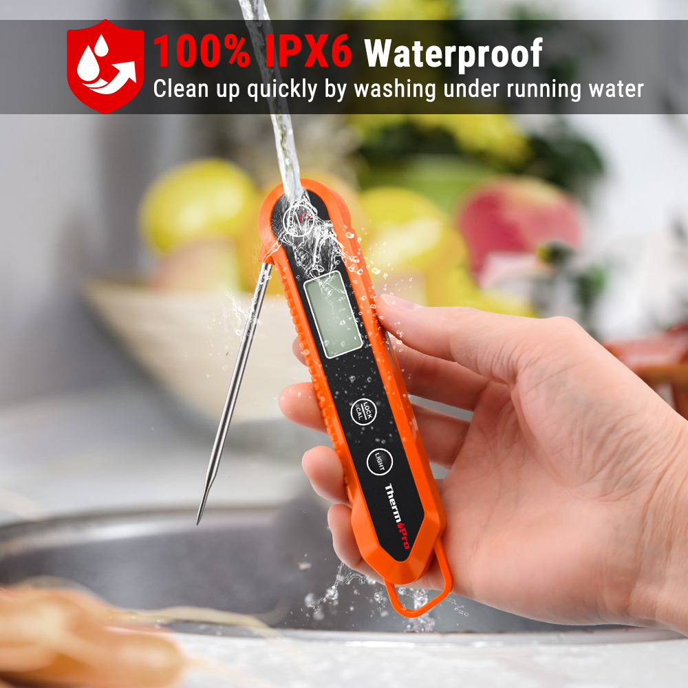Eine Hand hält ein oranges Thermometer unter fließendes Wasser in einer Küche.