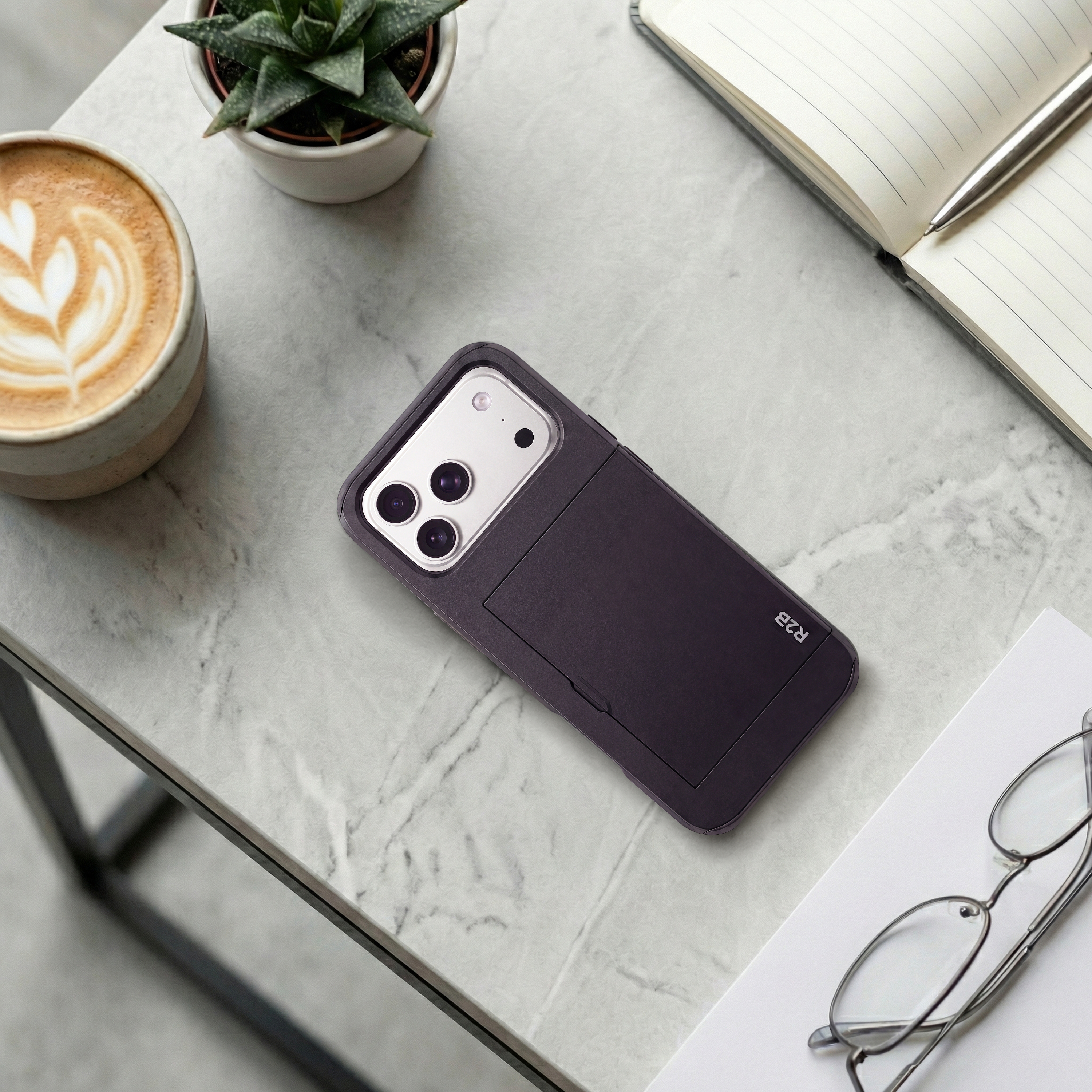 Ein Smartphone in einer dunkelvioletten Hülle mit Kartenfach liegt auf einem Marmortisch neben Kaffee, Notizbuch und Brille.