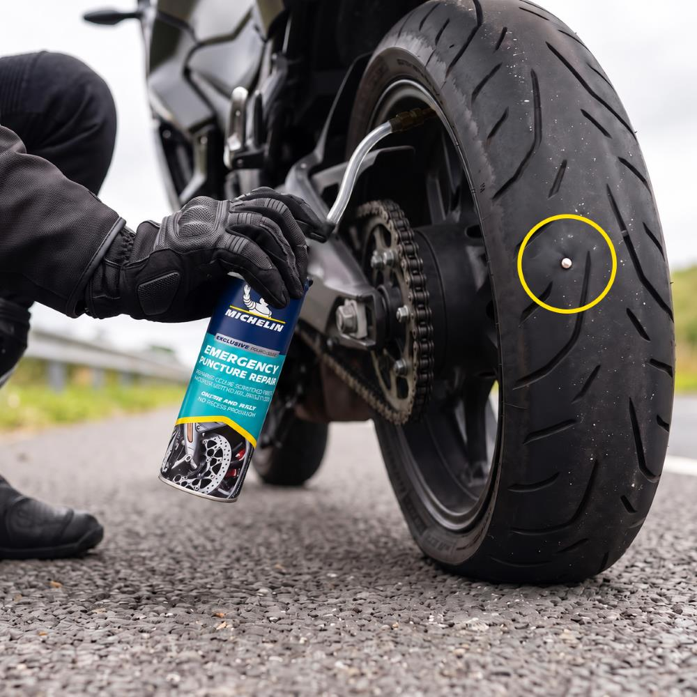 Bir kişi motosiklet lastiğine Michelin tamir spreyi sıkıyor.