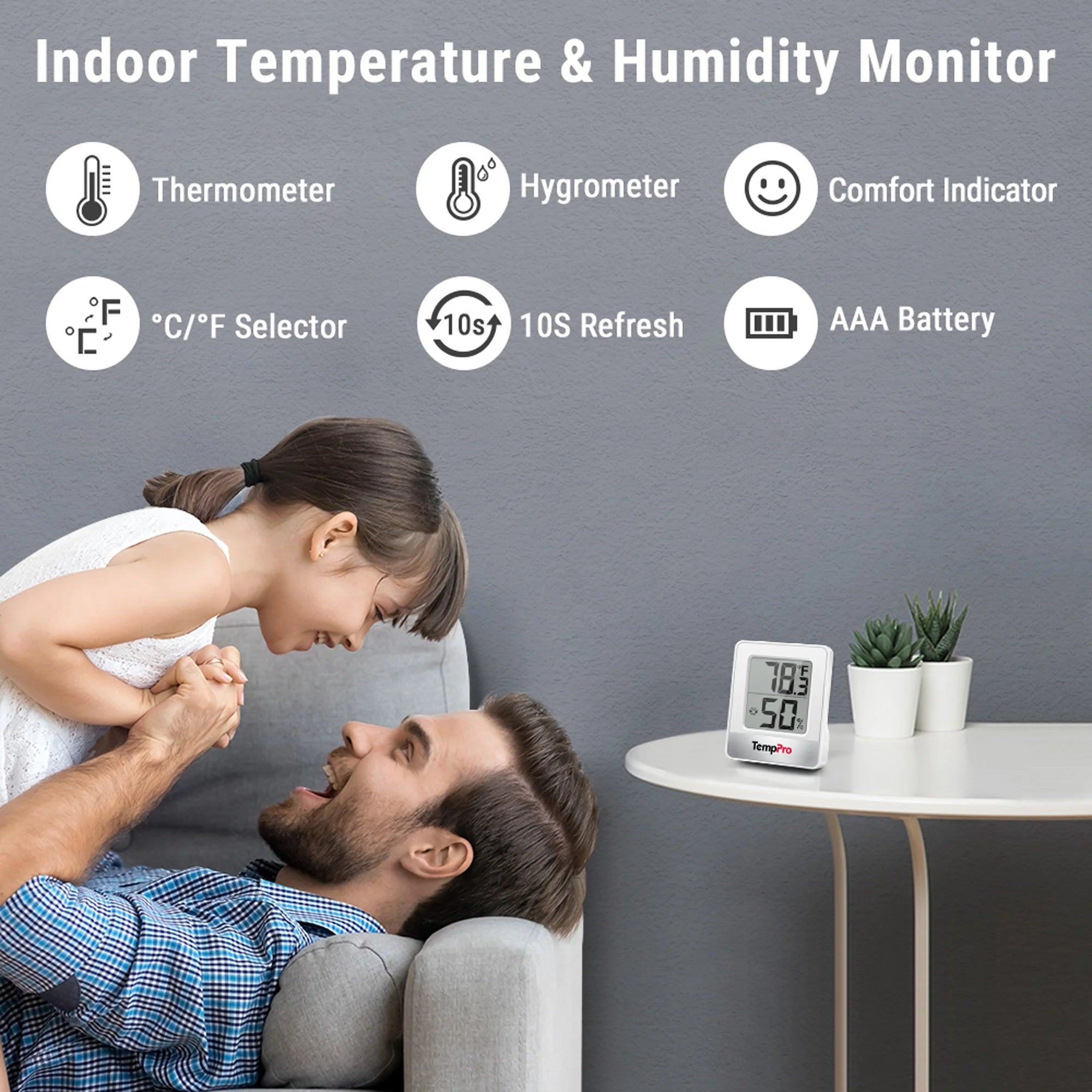 Ein Vater hebt lächelnd seine Tochter auf dem Sofa hoch, daneben steht ein Temperatur- und Feuchtigkeitsmonitor.