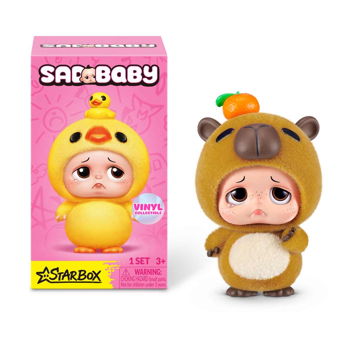 Figura de vinilo Sad Baby Capibara con una mandarina en la cabeza, junto a una caja rosa con un pato amarillo.