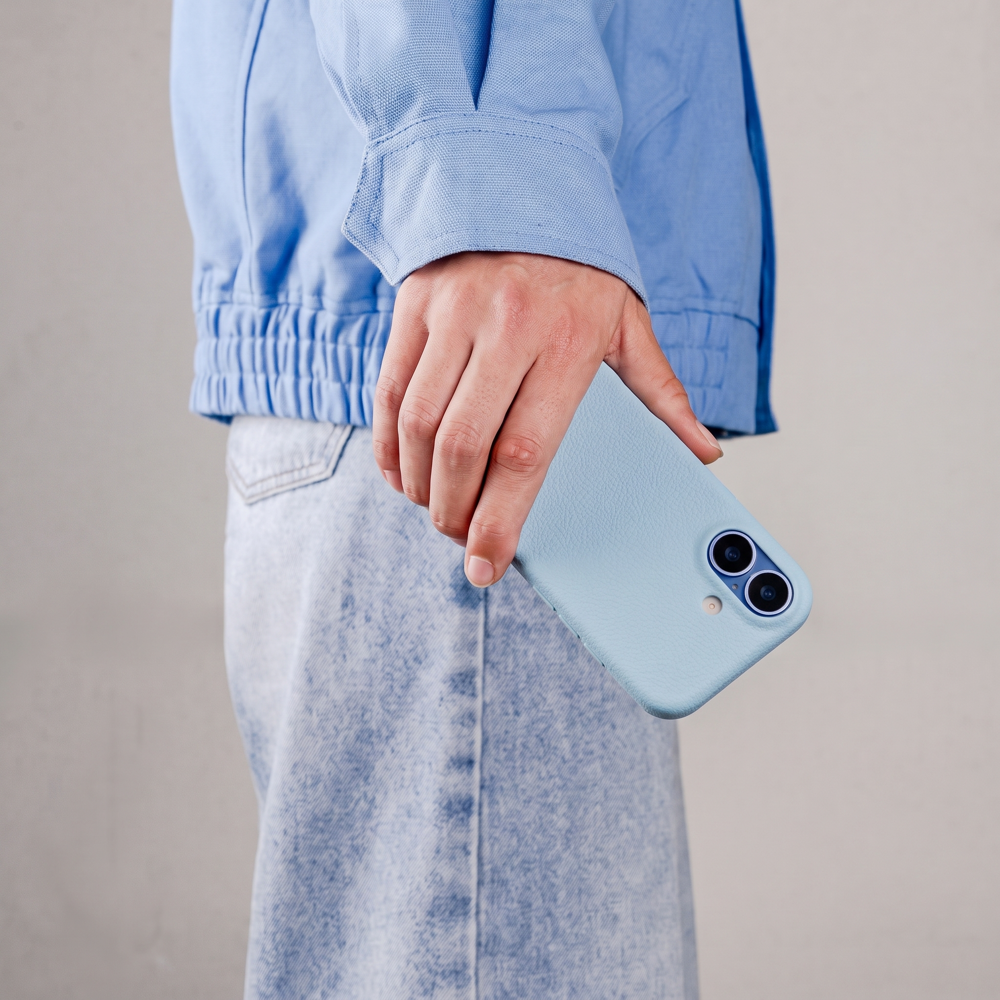 Persoon in lichtblauwe jas en jeans houdt een lichtblauwe smartphone met twee camera's vast.