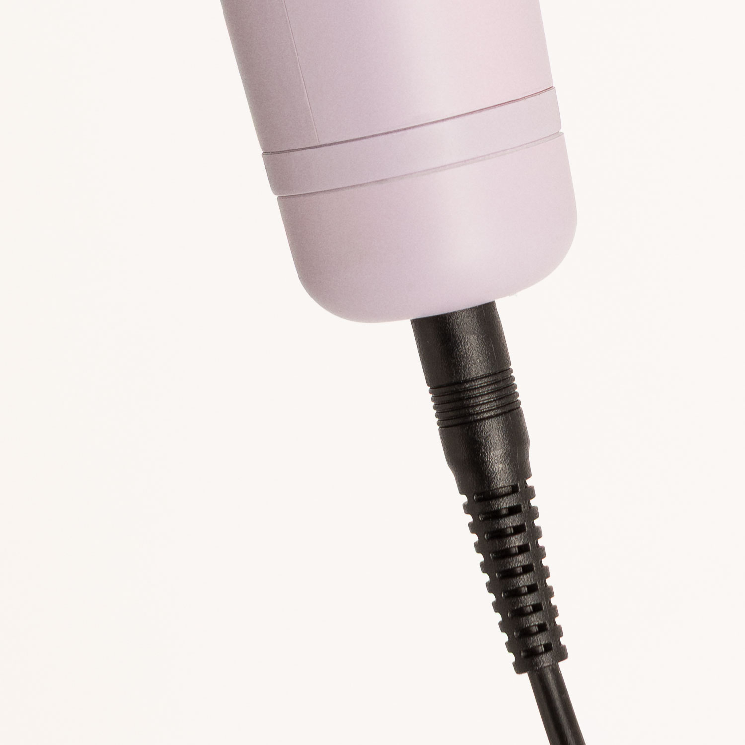 Un cable de alimentación negro está enchufado en la parte inferior de un dispositivo rosa claro sobre un fondo blanco.
