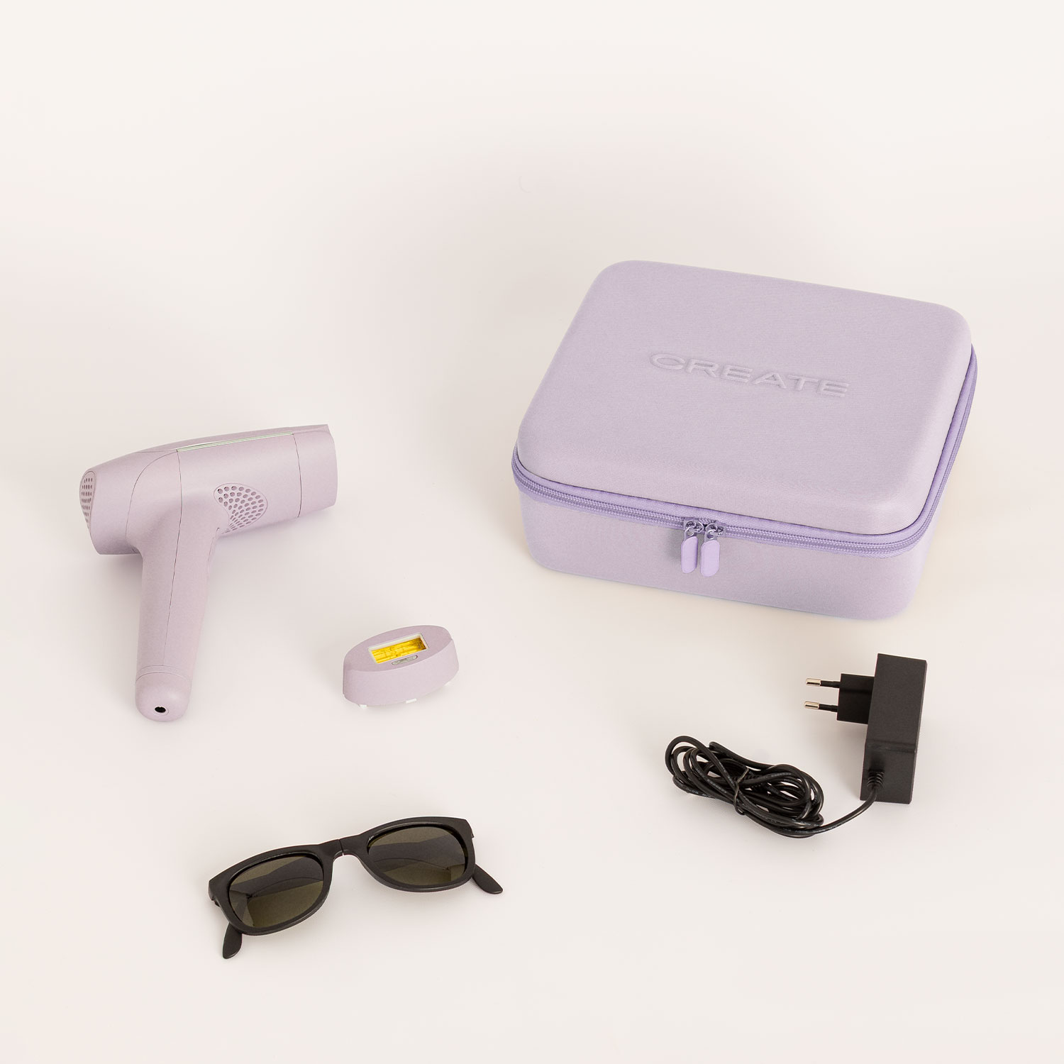 Un dispositivo de depilación morado, gafas, adaptador de corriente y estuche morado sobre una superficie clara.