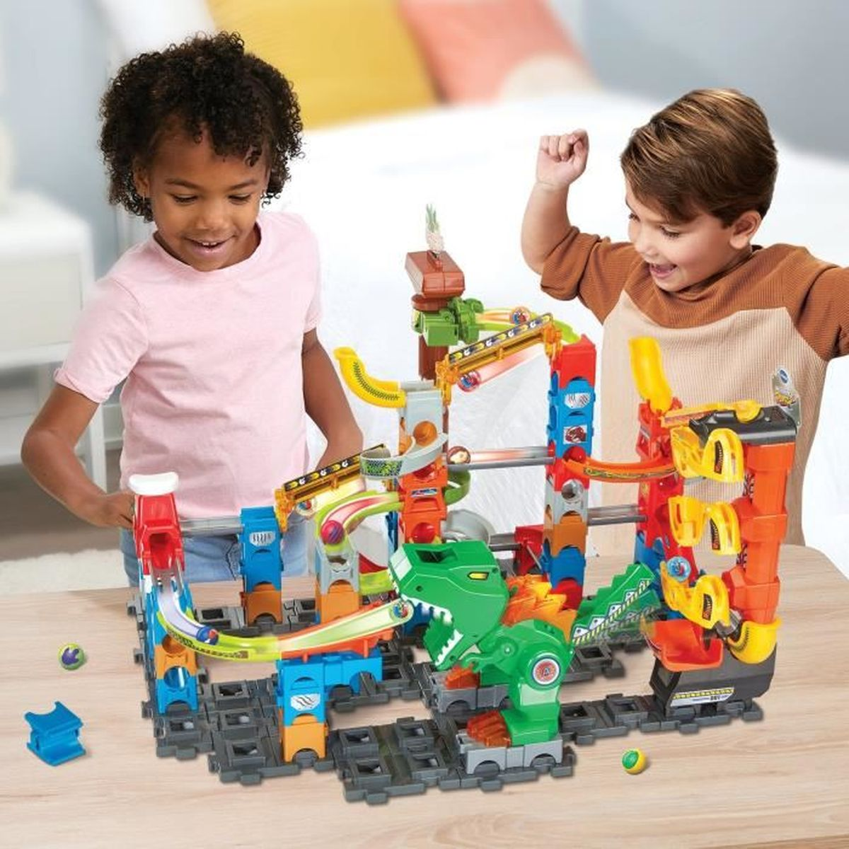 Zwei Kinder lächeln und spielen zusammen mit einer bunten Murmelbahn an einem Holztisch.