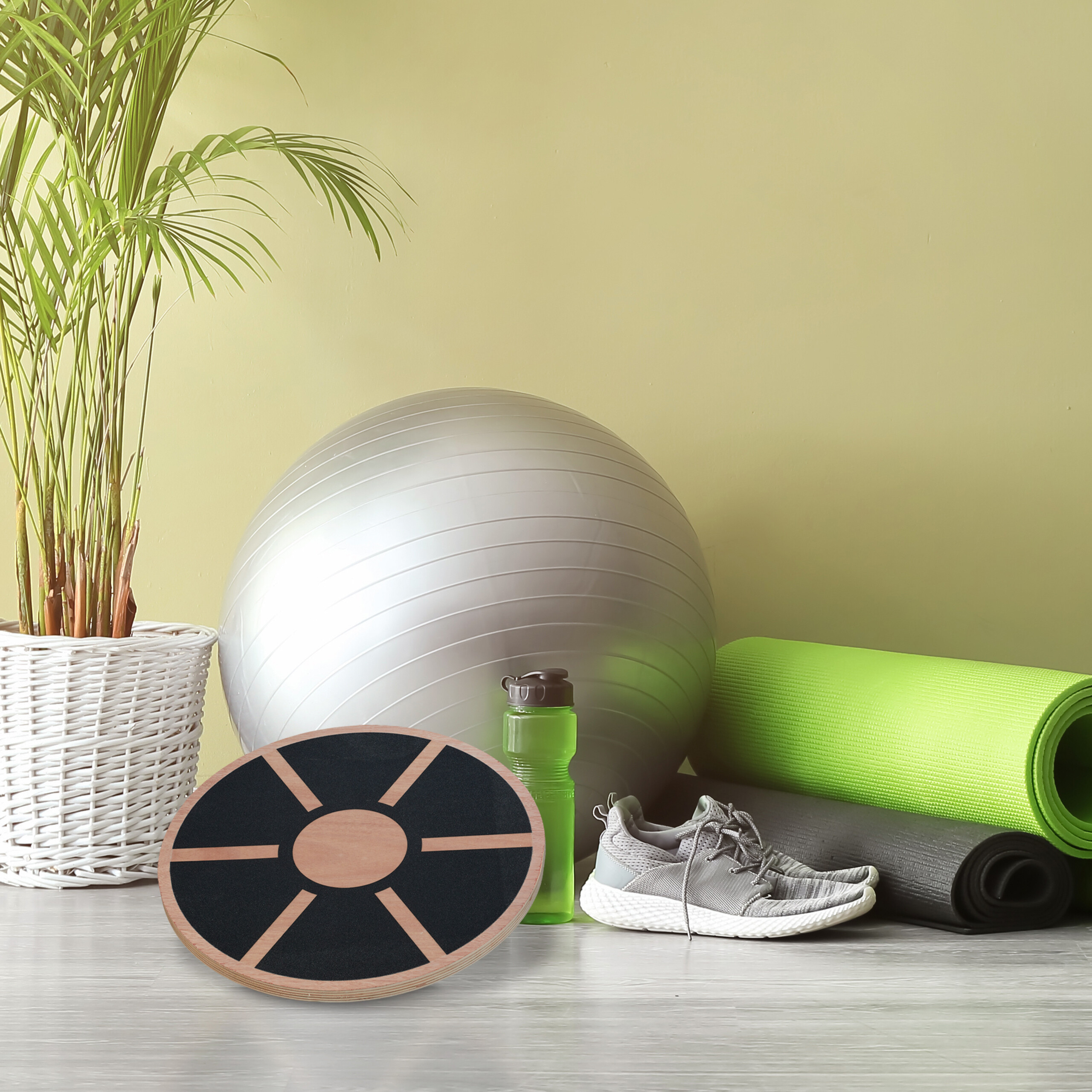 Fitnessgeräte mit Gymnastikball, Balanceboard, Yogamatten, Schuhen, Wasserflasche und Topfpflanze.