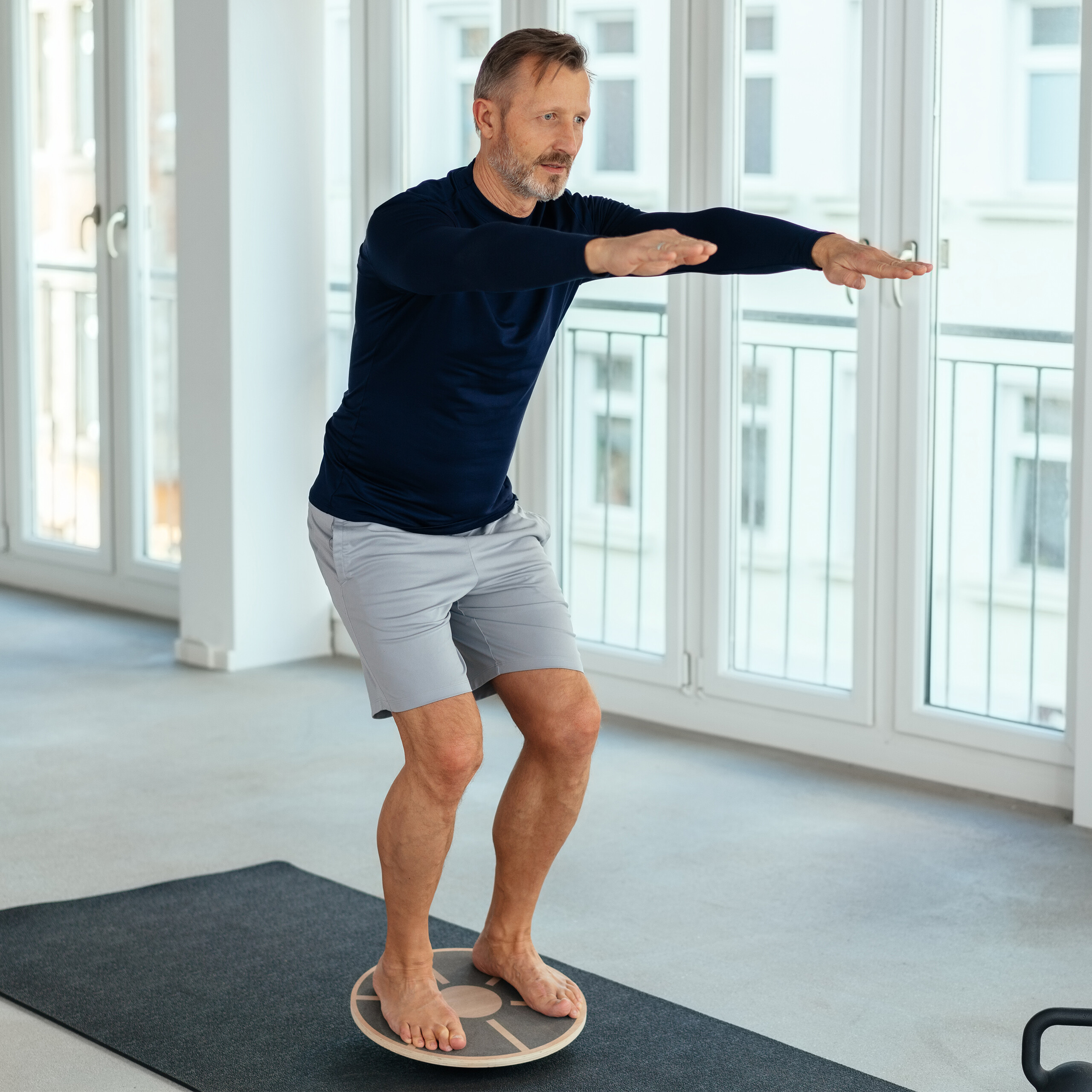 Ein reifer Mann in blauem Hemd und grauen Shorts balanciert auf einem Holzbrett.
