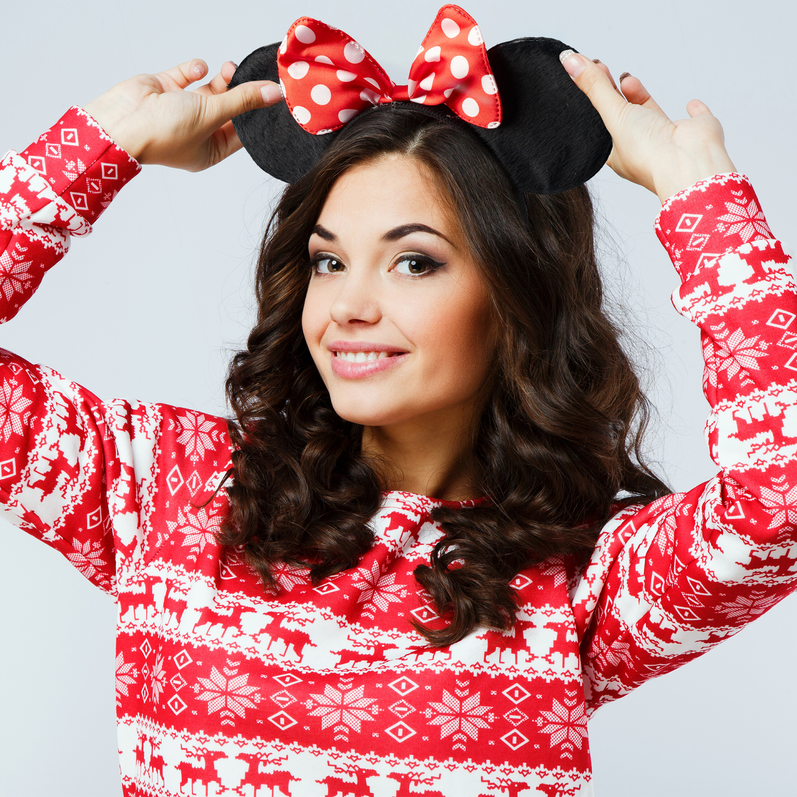 Eine lächelnde Frau in einem roten Weihnachtspullover trägt einen Haarreif mit schwarzen Ohren und einer roten Schleife.