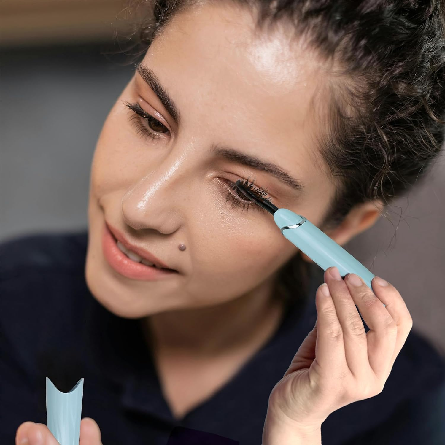 Eine Frau verwendet eine hellblaue beheizbare Wimpernzange an ihren Wimpern.