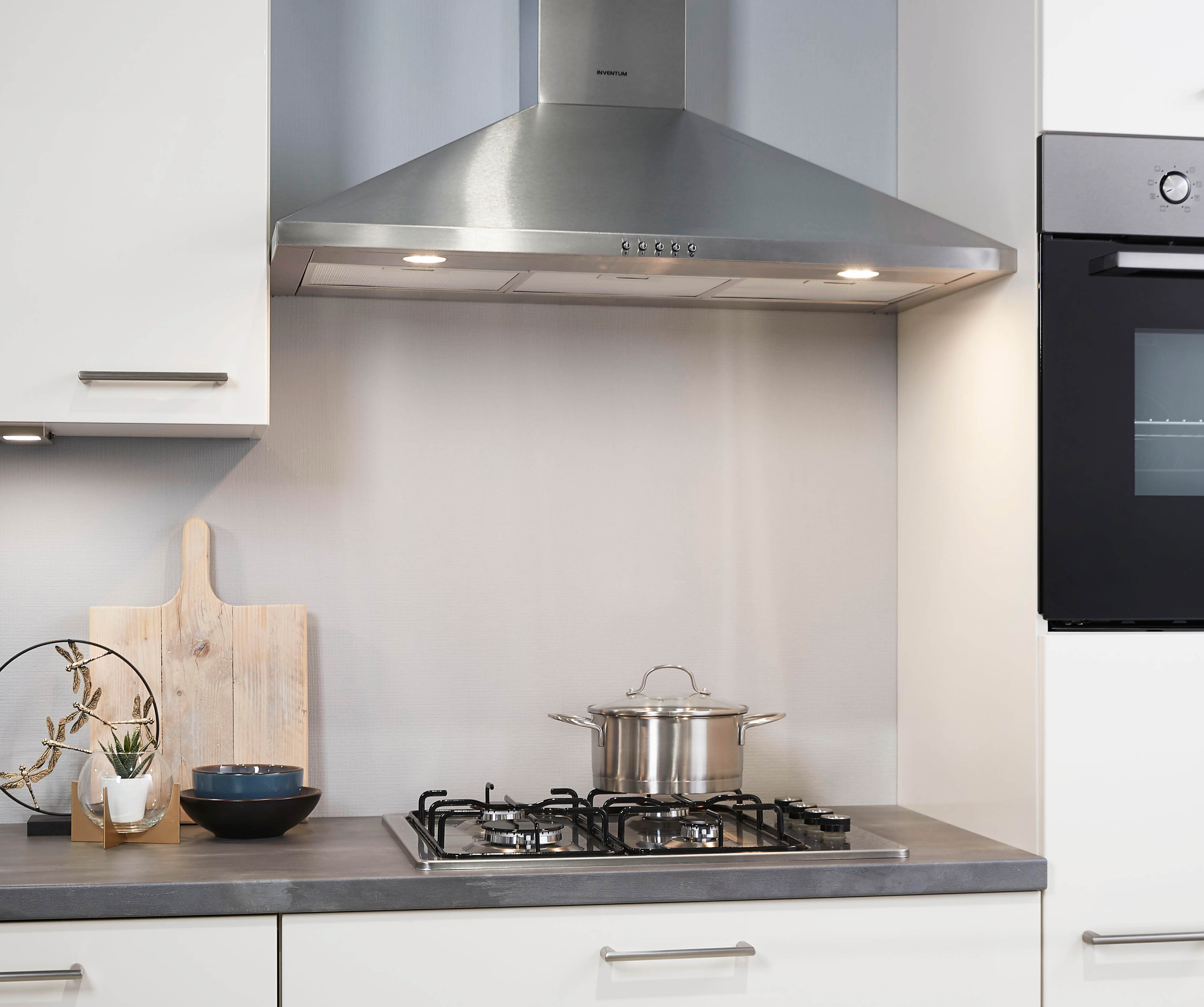 A modern kitchen counter with a gas stove, pot, cutting board, and a stainless steel range hood above.