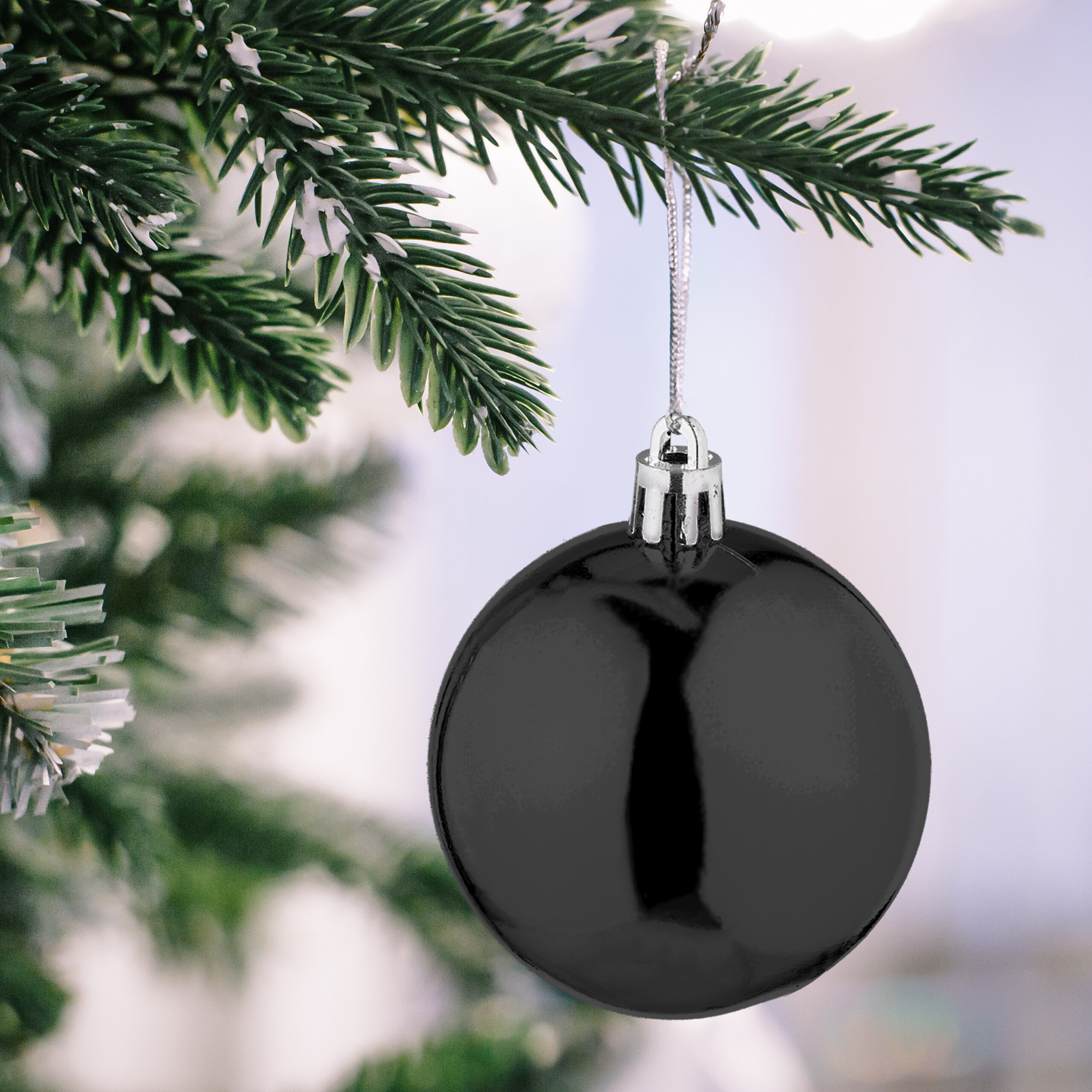 Eine glänzende schwarze Christbaumkugel hängt an einem verschneiten Zweig.