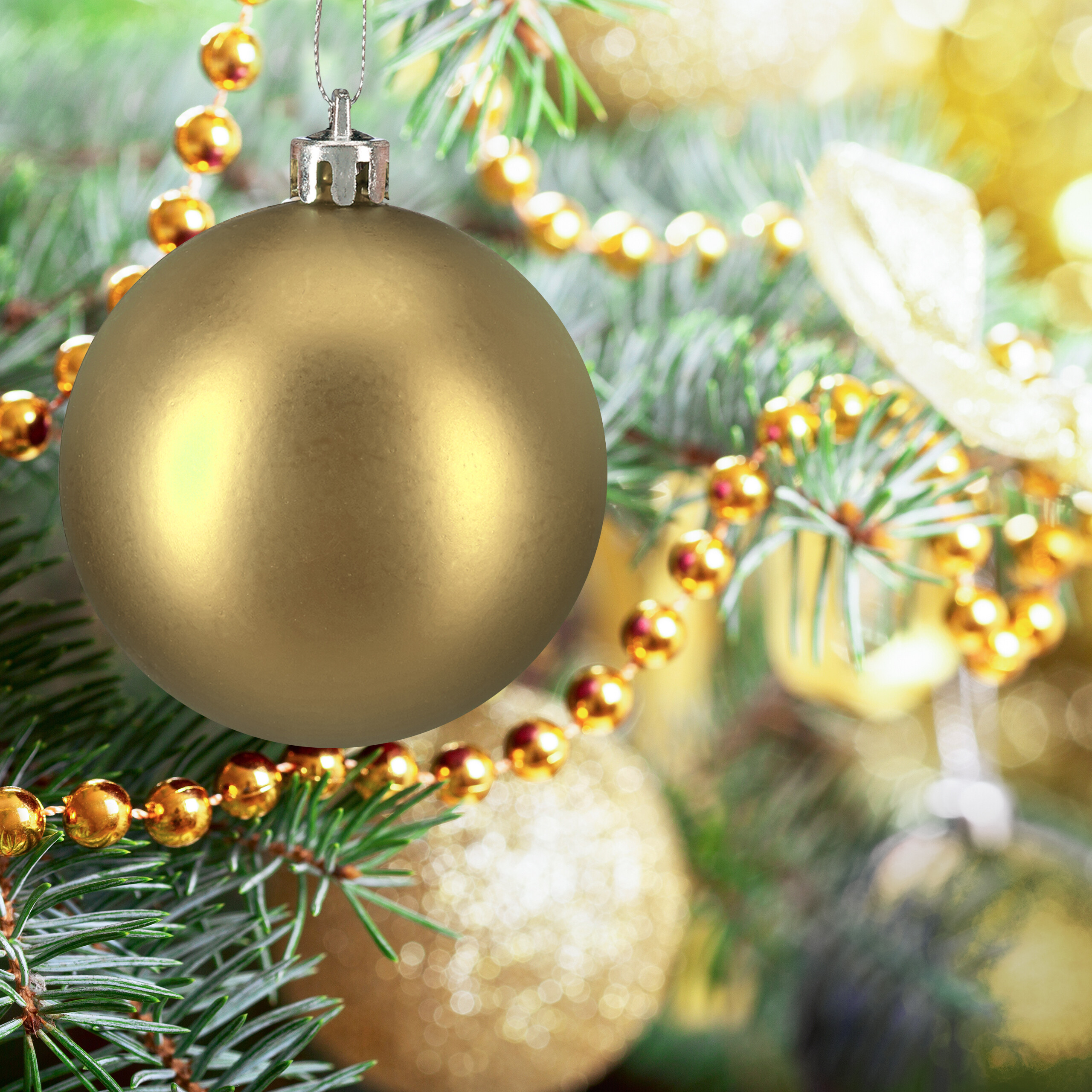 Eine glänzende goldene Weihnachtskugel hängt an einem grünen Tannenbaum mit goldenen Perlenketten.