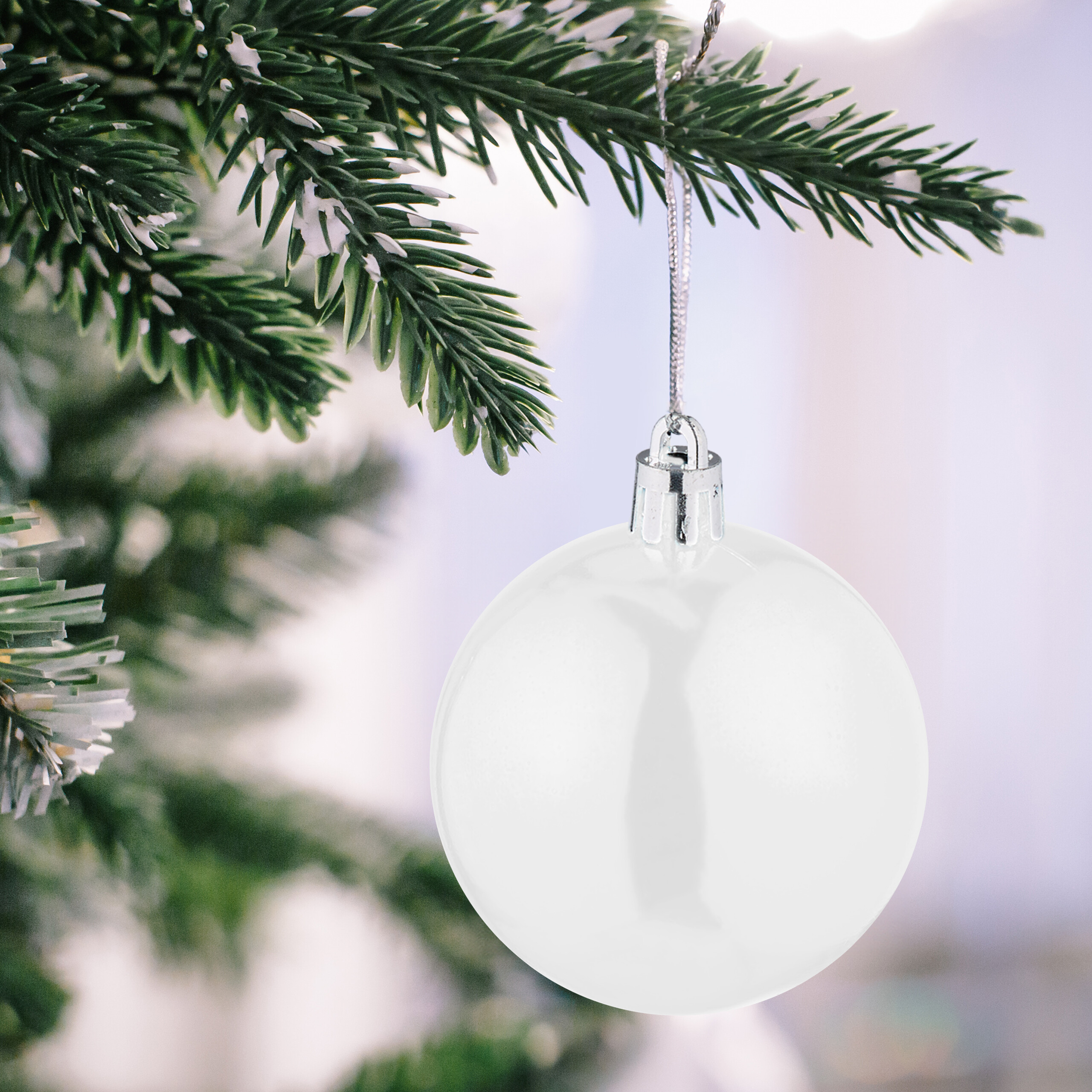 Eine glänzende weiße Christbaumkugel hängt an einem grünen Tannenzweig.