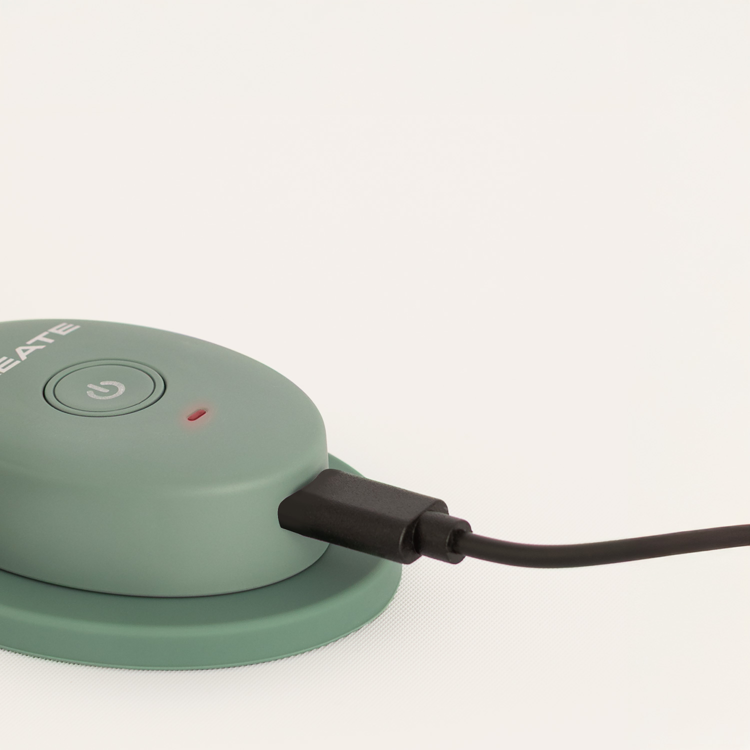 Un dispositivo electrónico verde en una base con un cable de carga negro conectado y una luz LED roja.