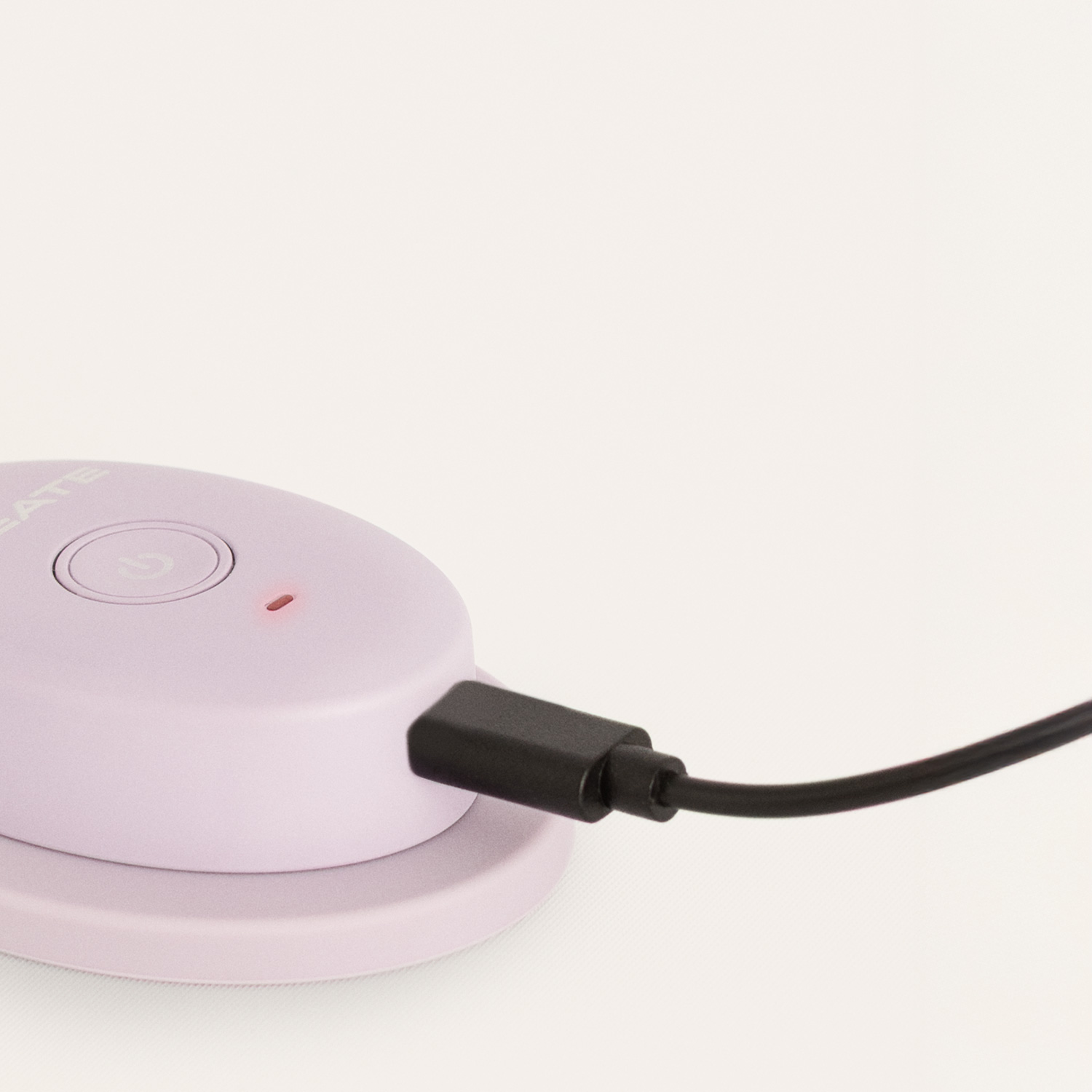 Un dispositivo morado claro conectado a un cable de carga negro sobre fondo liso.