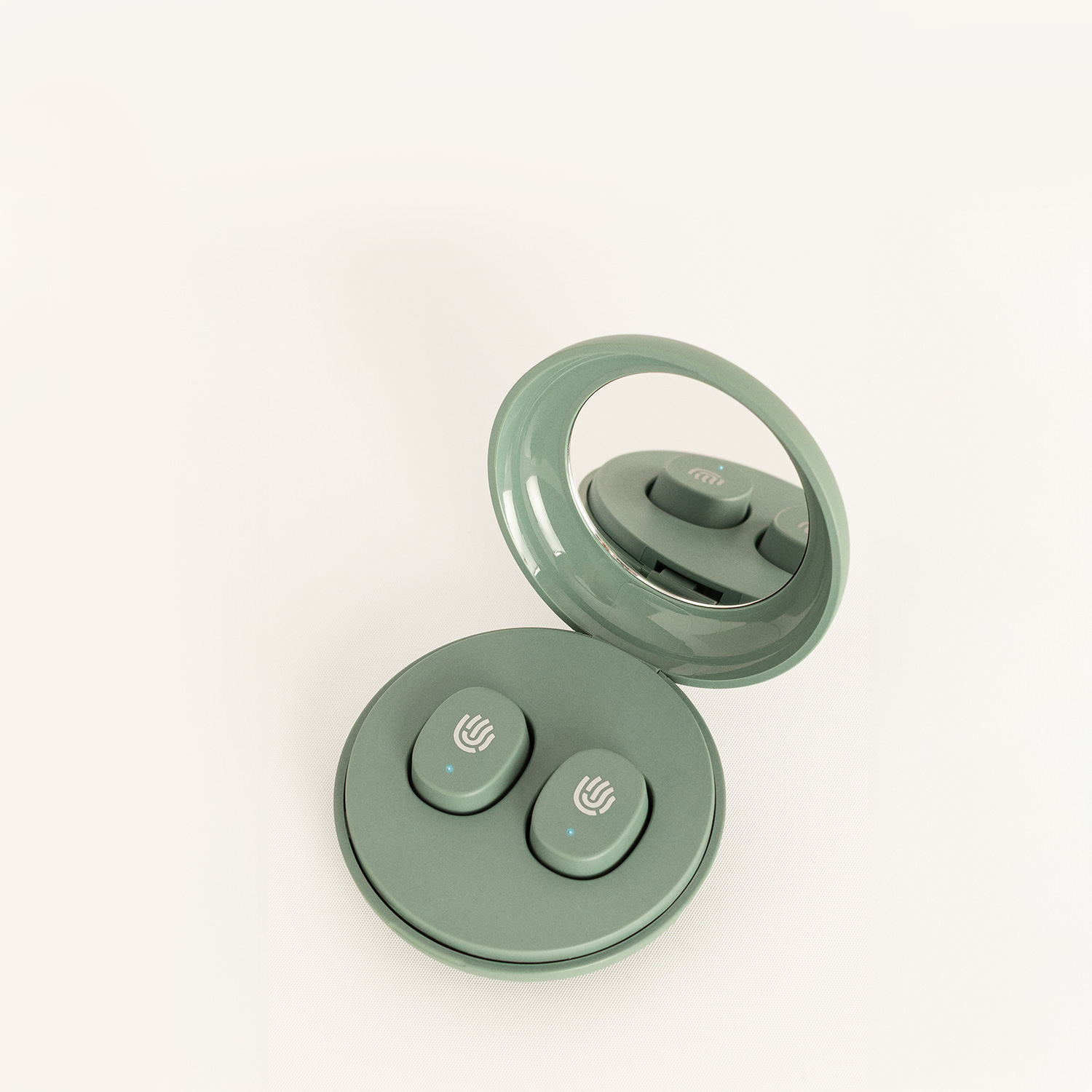 Un estuche de carga redondo verde salvia con dos auriculares inalámbricos dentro, sobre un fondo blanco.